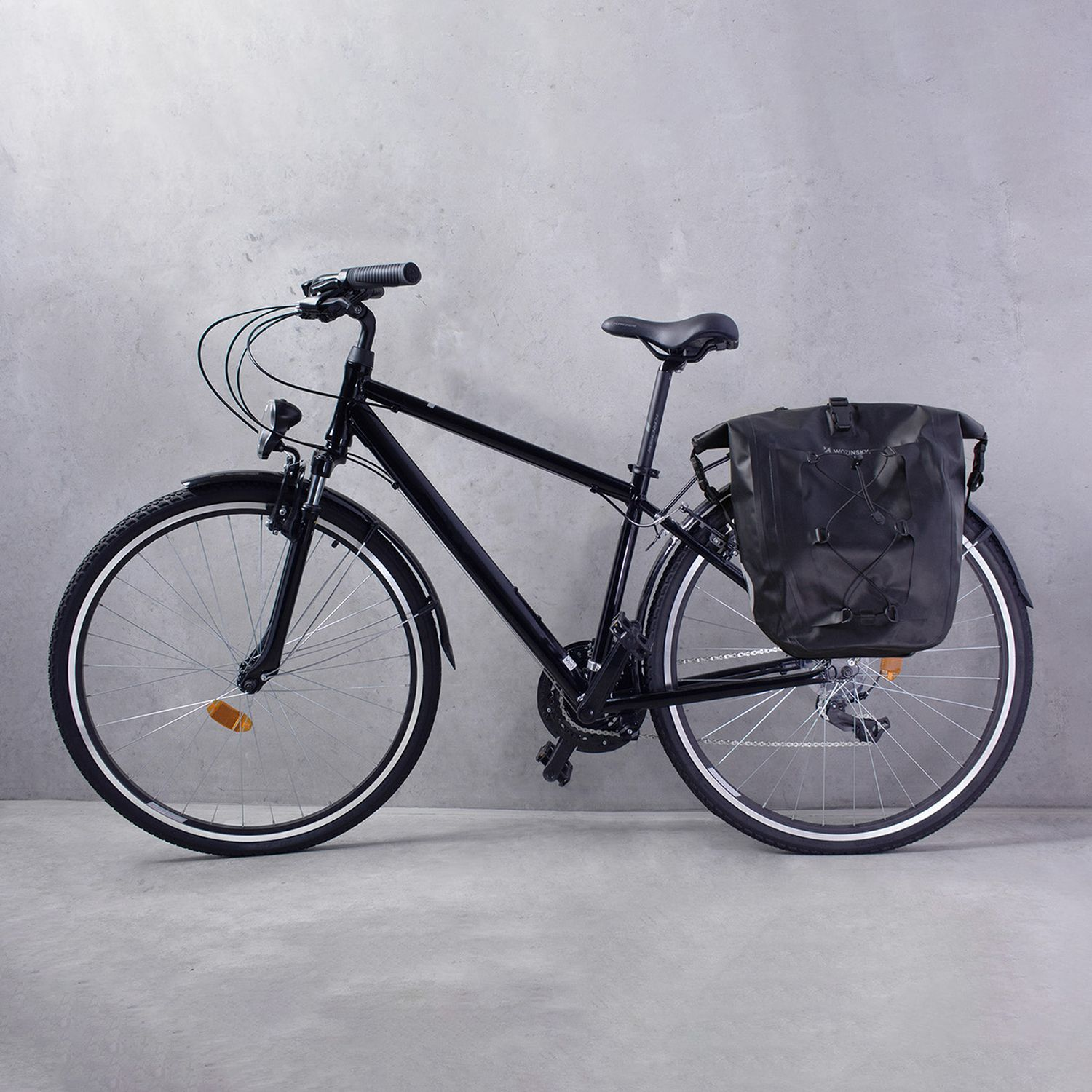 Schwarzes Fahrrad mit schwarzer Tasche am Heck. Grauer Hintergrund.