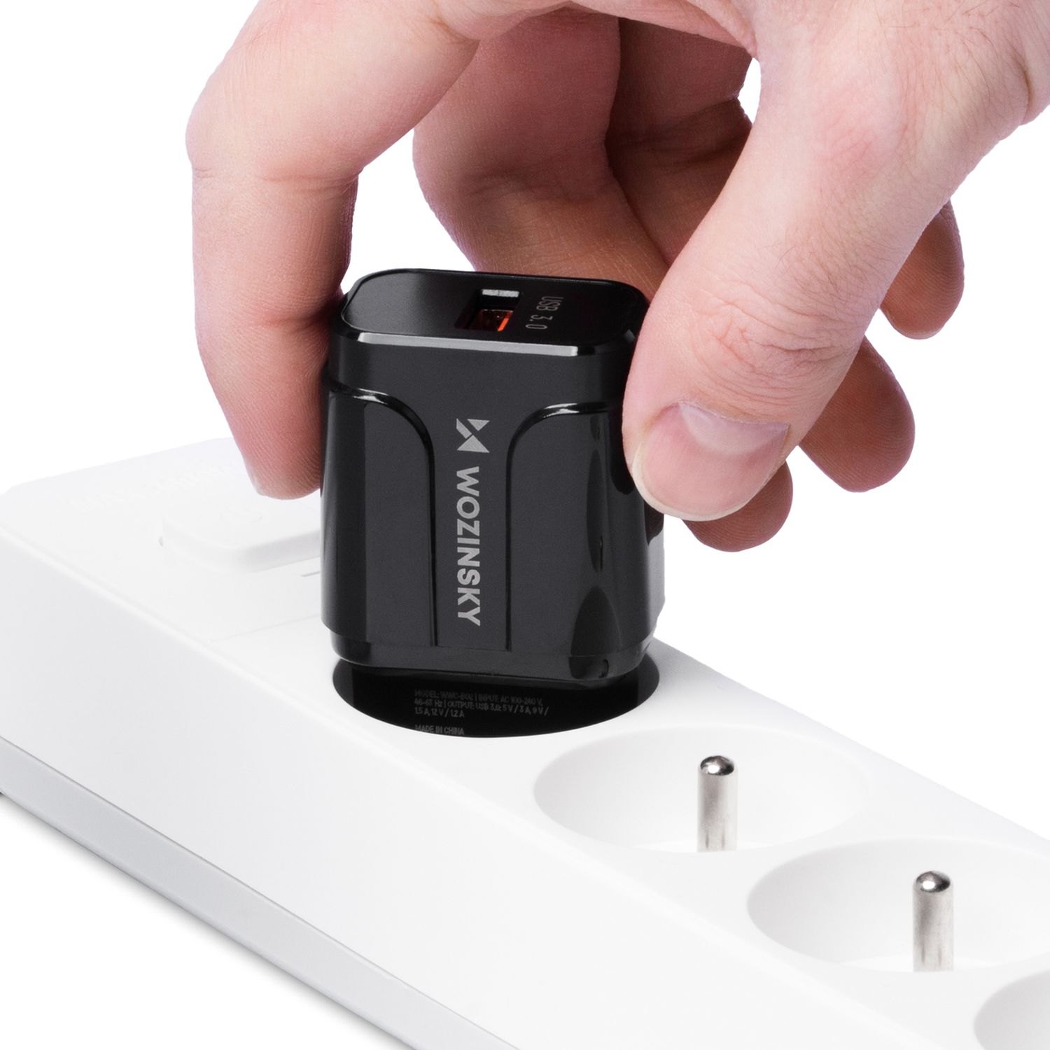 Eine Hand steckt ein schwarzes USB-Ladegerät in eine weiße Steckdosenleiste.