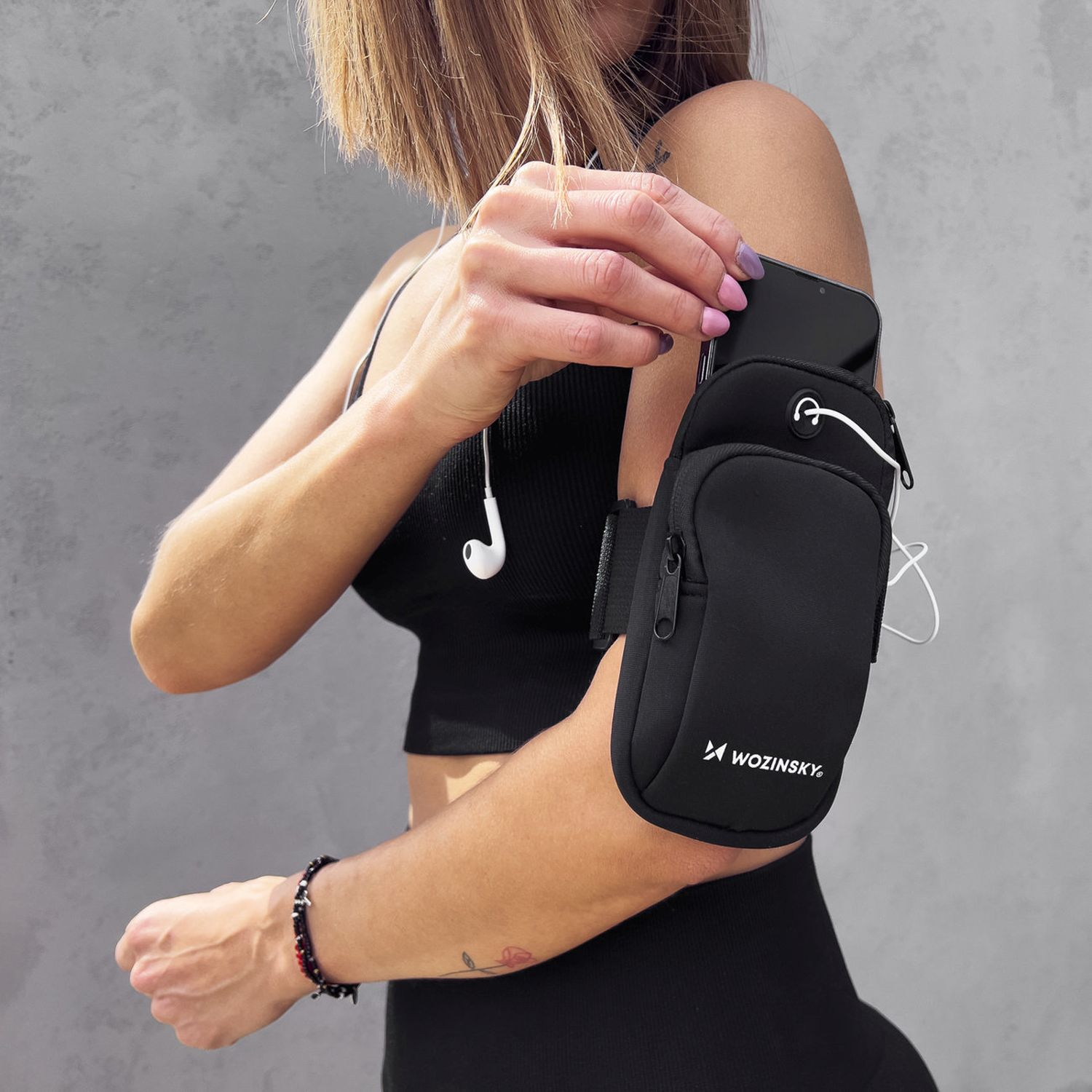 Eine Frau trägt eine schwarze Armbinde mit einem Telefon darin. Sie ist draußen mit Ohrhörern.