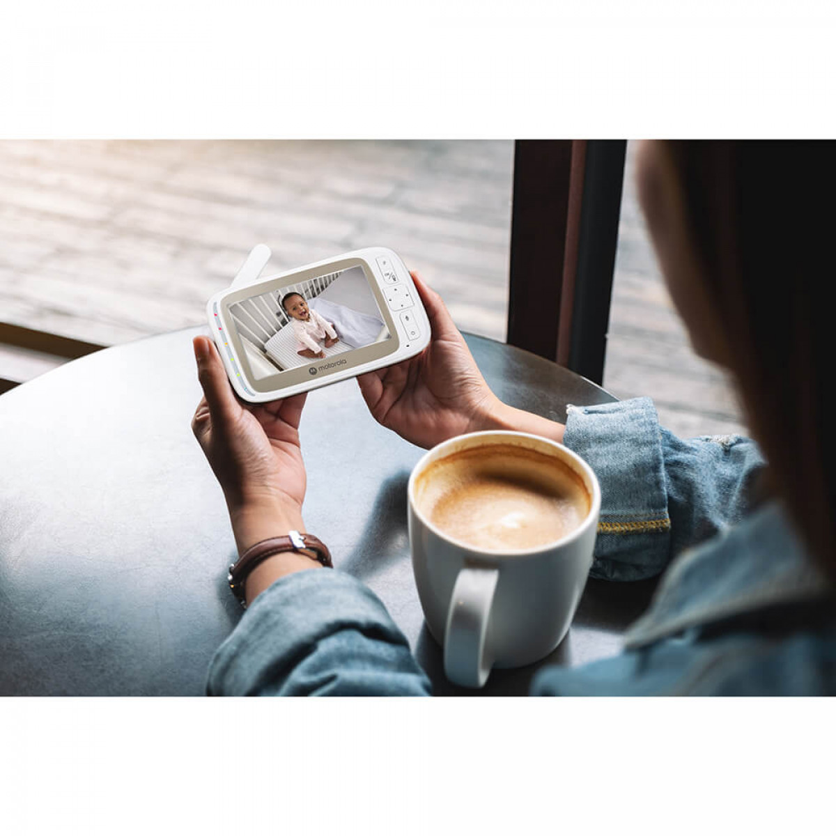 Eine Frau hält einen Babyphone, das ein Baby in einem Kinderbett zeigt.