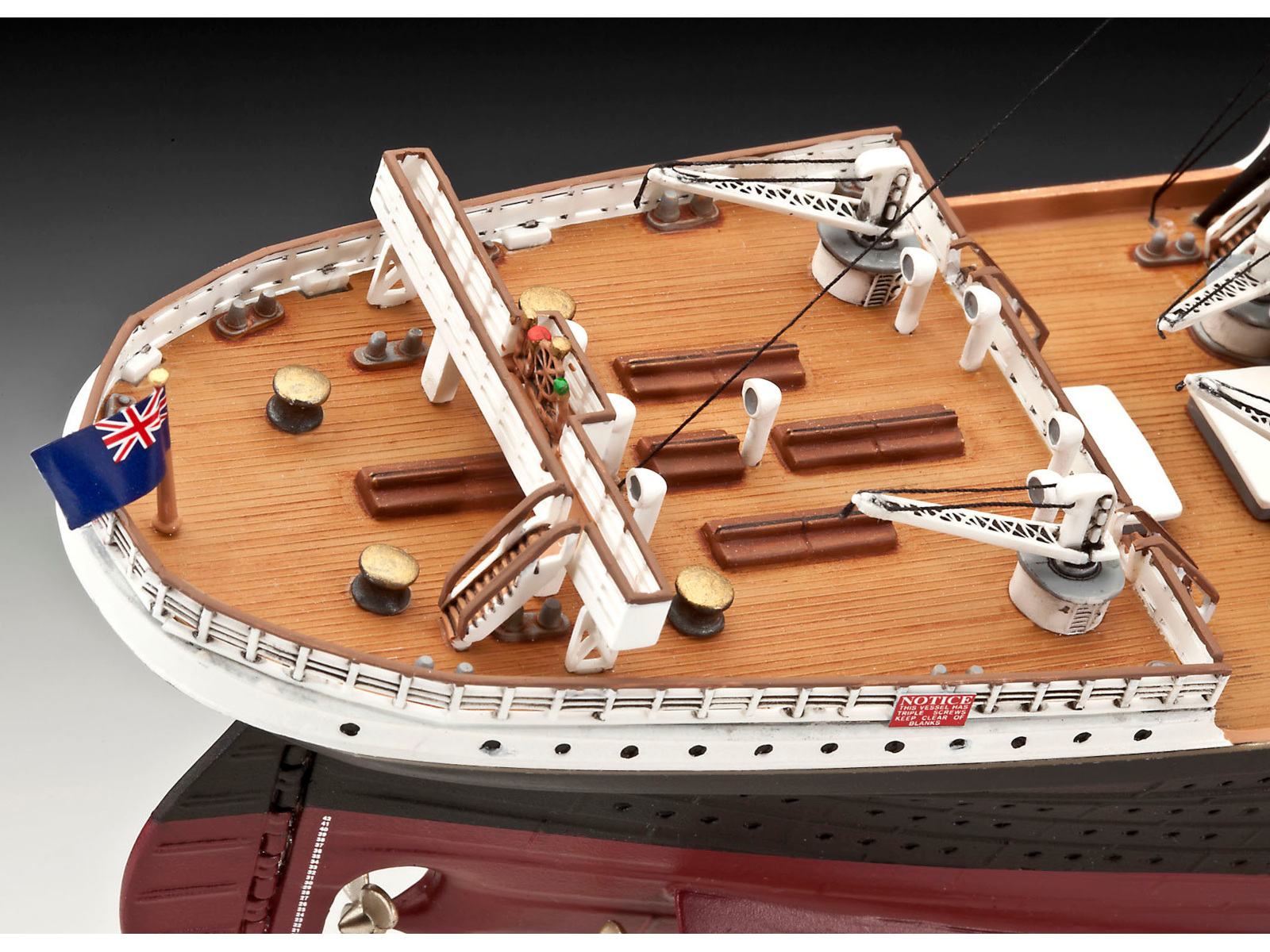Modellschiffdeck mit weißen und braunen Details, einer Flagge und kranartigen Strukturen.