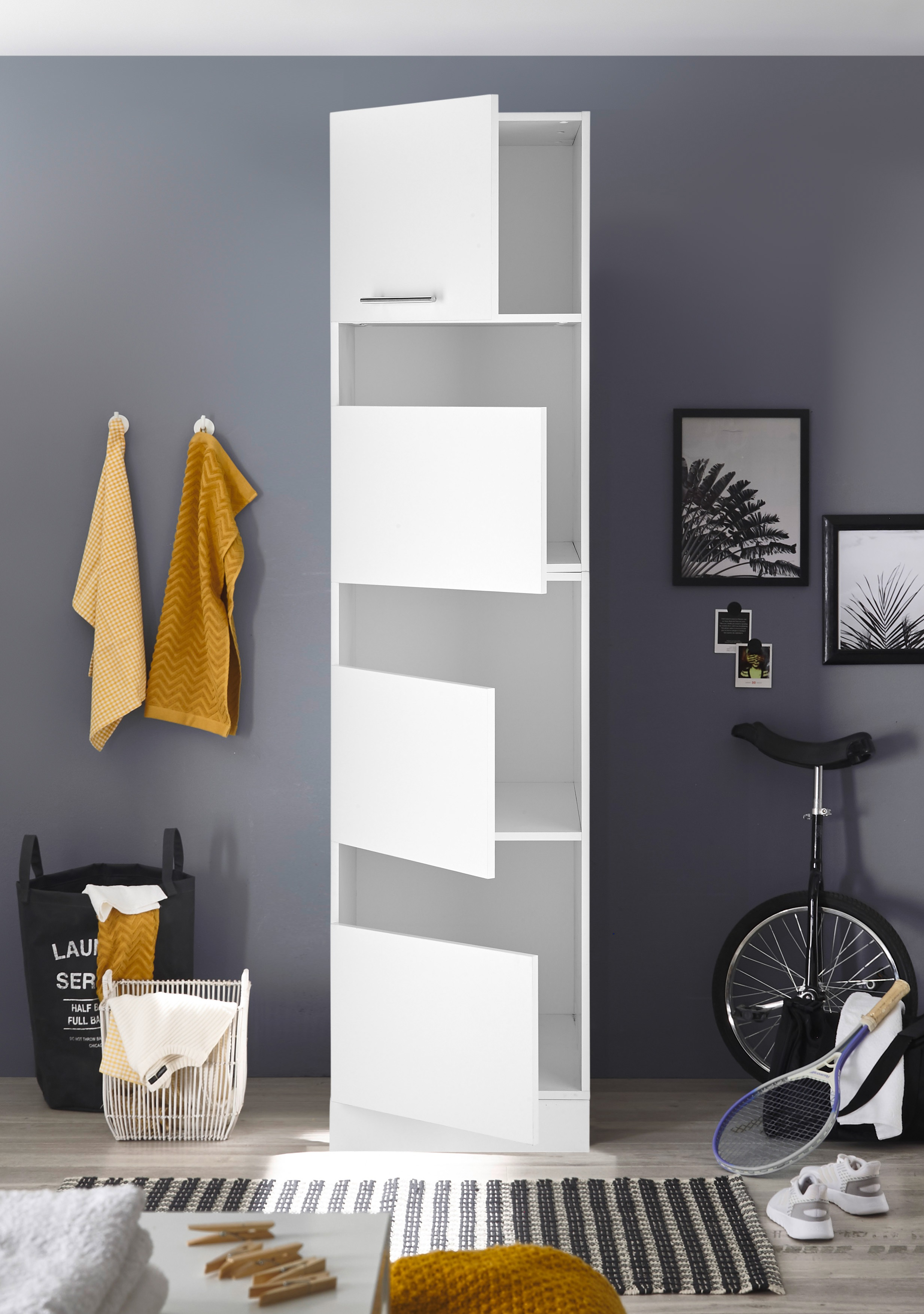 Weißer hoher Schrank mit offenen Türen, Handtüchern, Einrad und Wäschekorb in einem Raum.