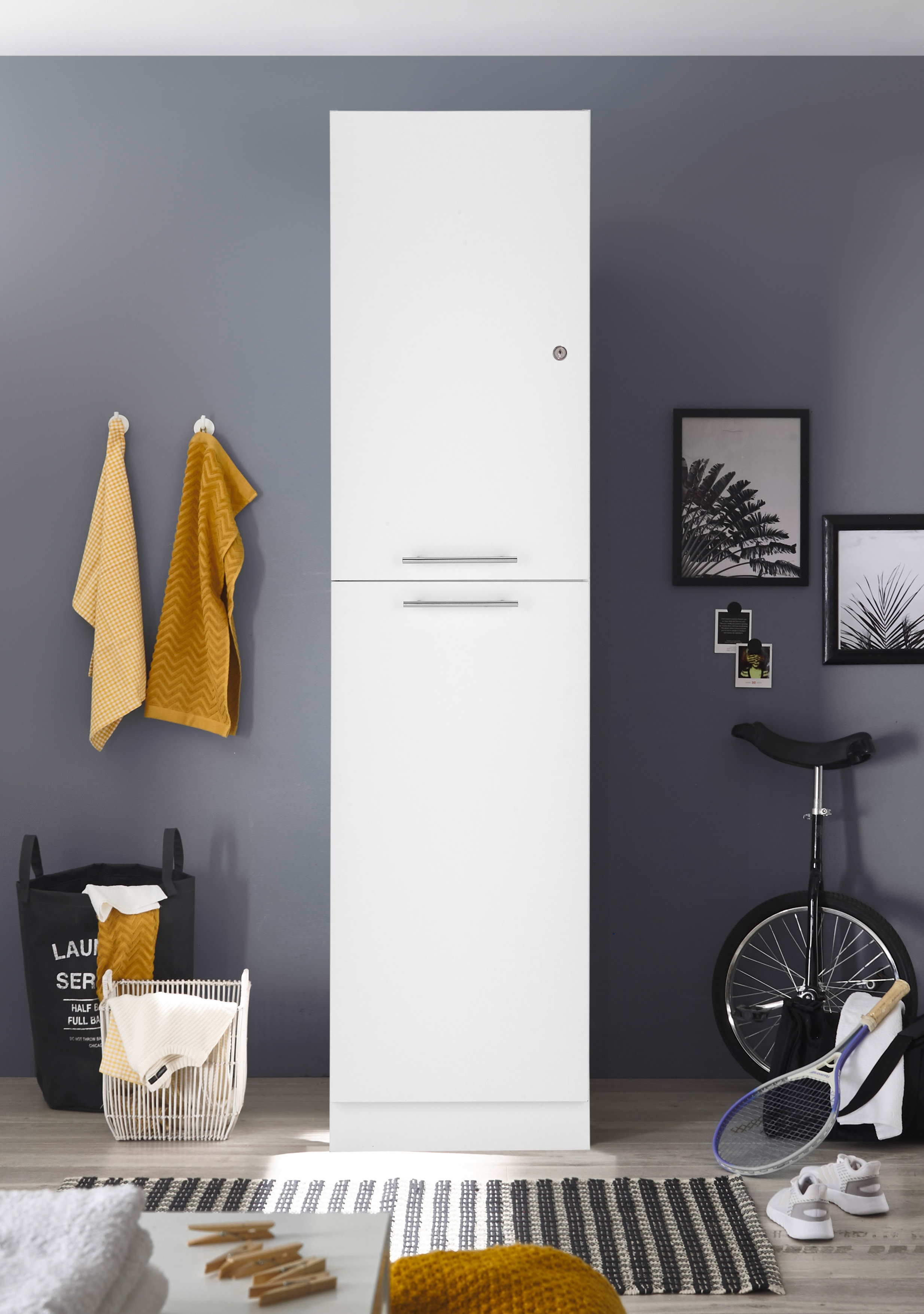 Weißer hoher Schrank in einem Raum mit grauen Wänden, einem Einrad und einem Wäschekorb.