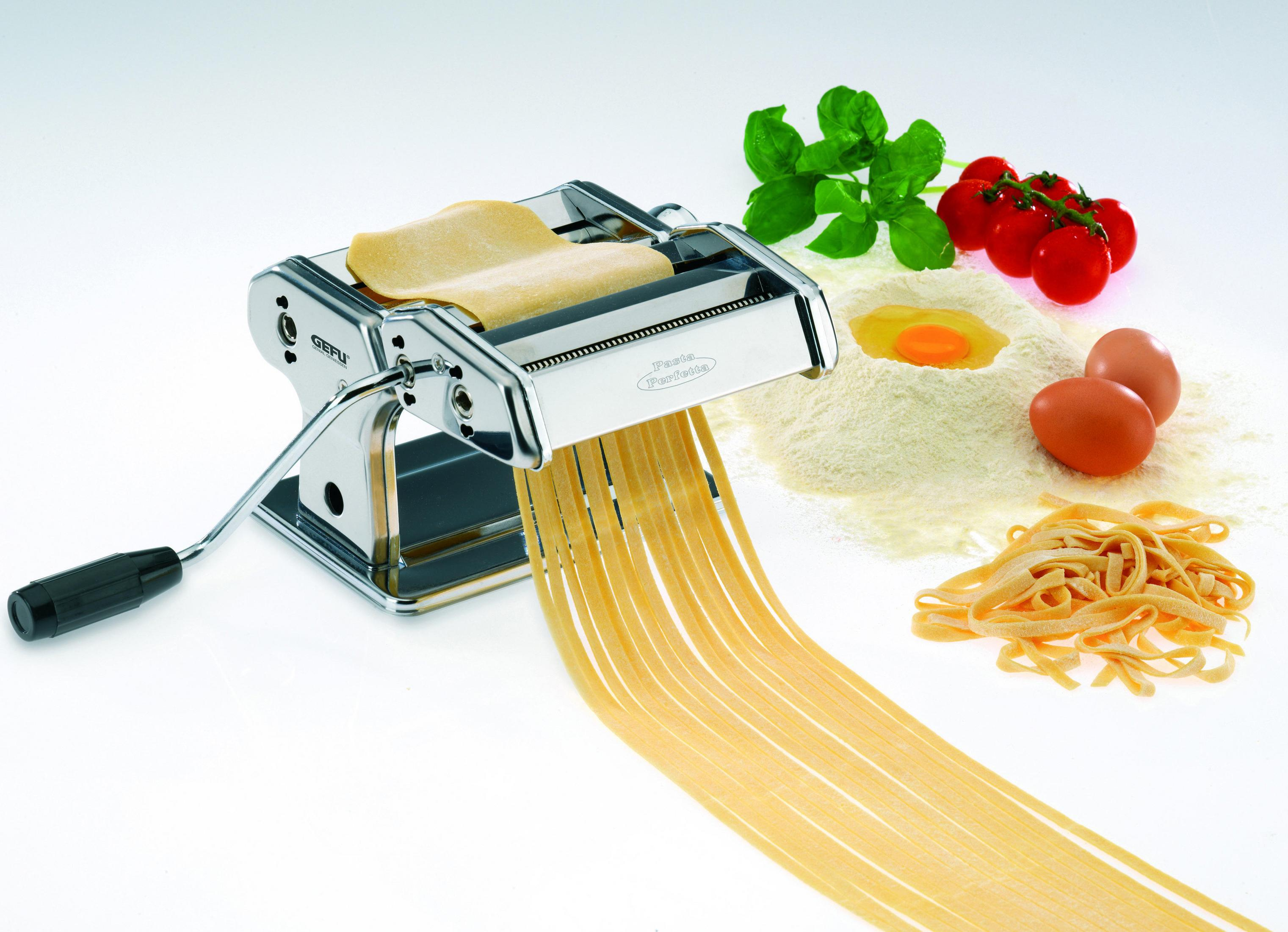 Pastamaschine mit Pasta und Zutaten. Mehl, Eier, Tomaten und Basilikum. Weißer Hintergrund.