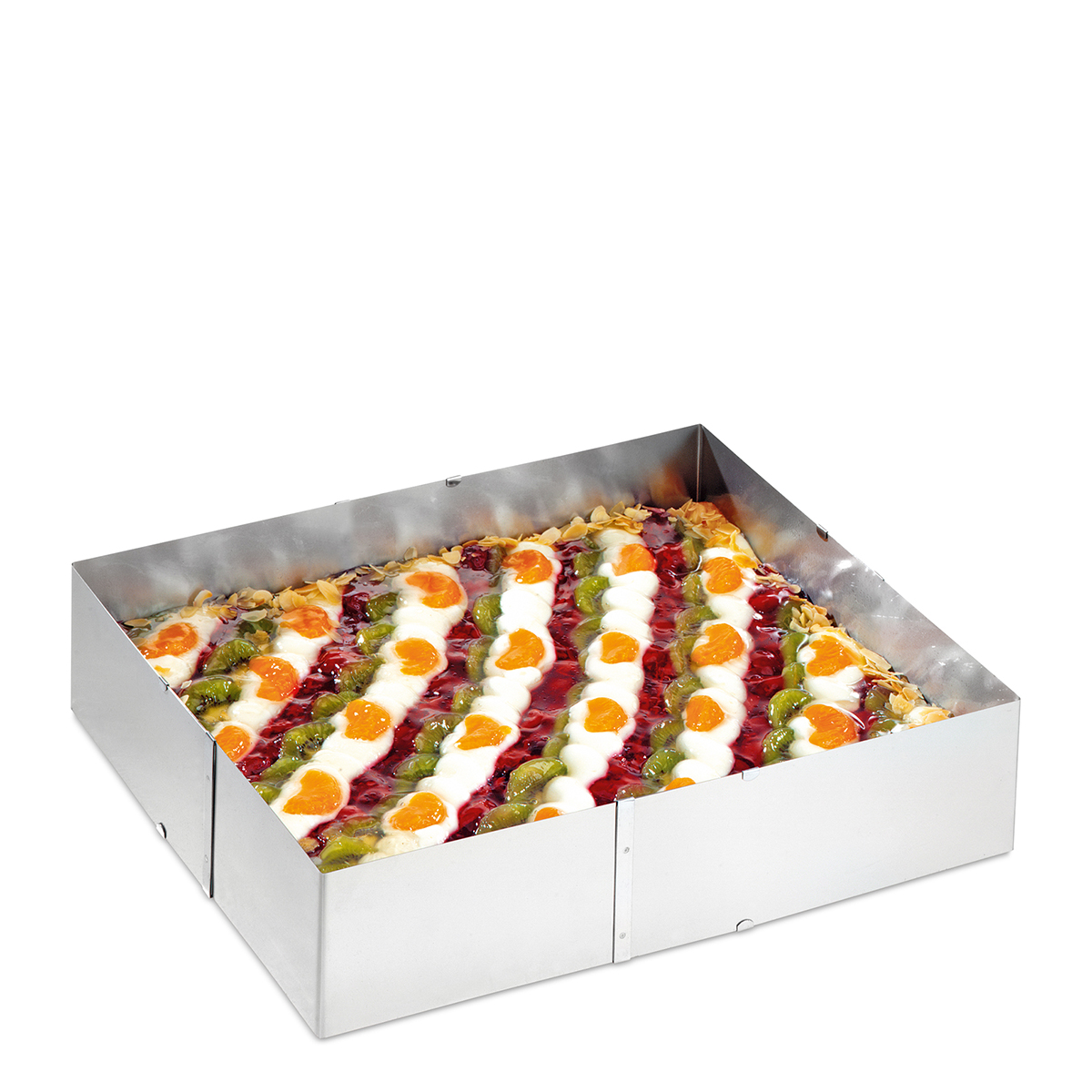 Gâteau dans un cadre métallique, avec garnitures de fruits et crème, sur fond blanc.