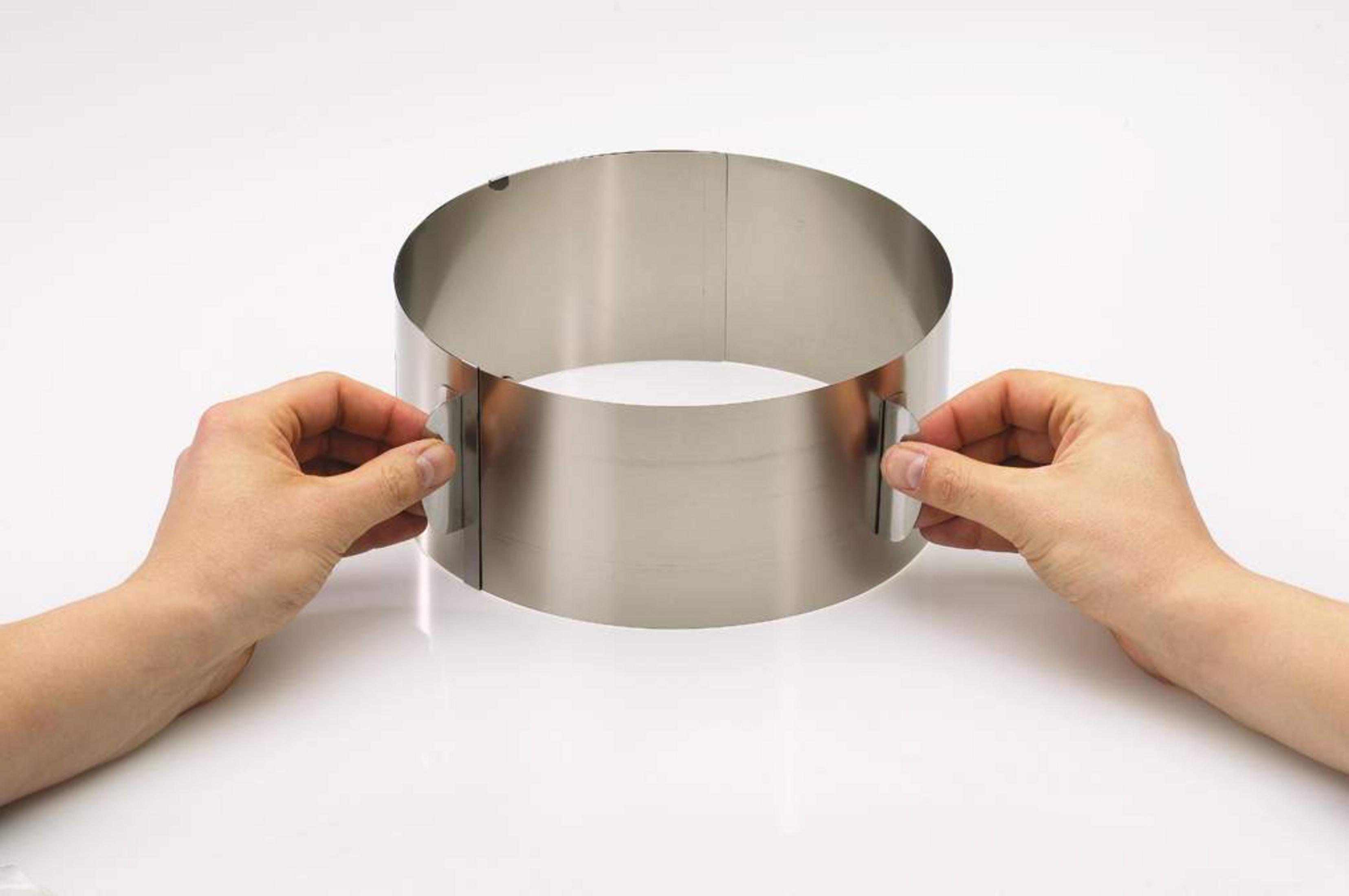 Mains ajustant un cercle à gâteau en acier inoxydable sur fond blanc.