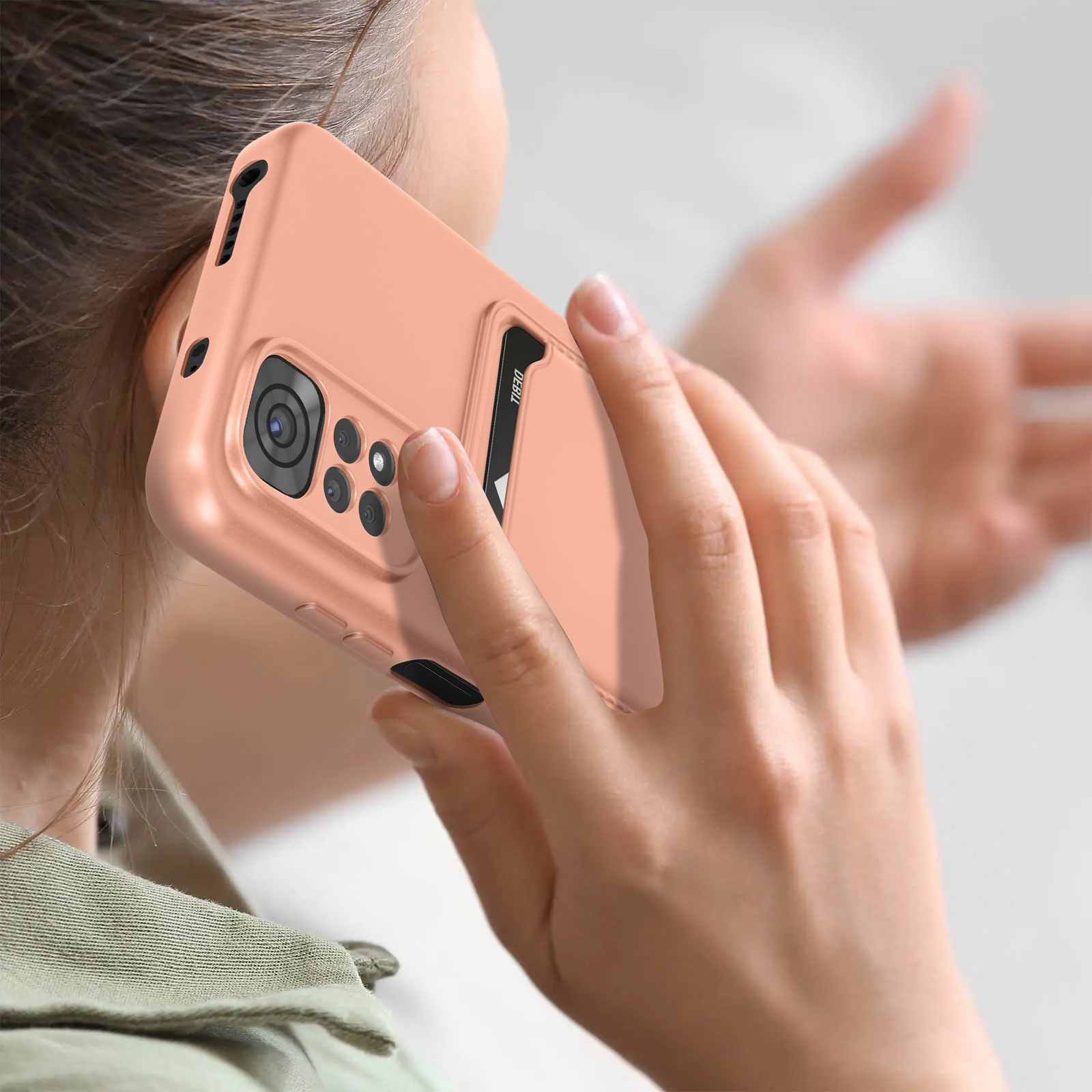 Eine Frau hält ein Telefon mit pfirsichfarbener Hülle an ihr Ohr. Die Hülle hat Kameras und einen Kartensteckplatz.