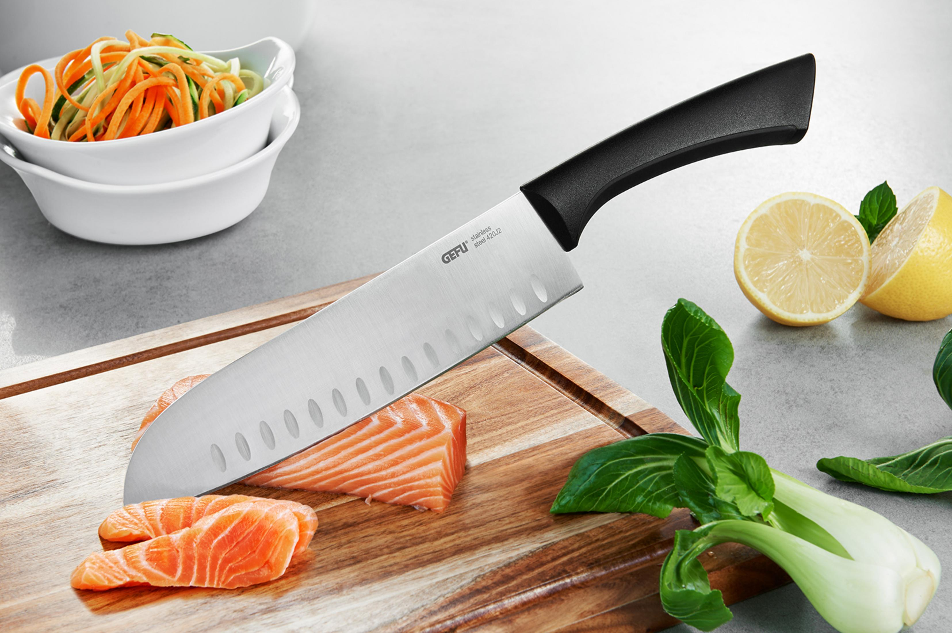 Ein Kochmesser auf einem Holzschneidebrett mit Lachs und Chinakohl neben einer Zitrone.