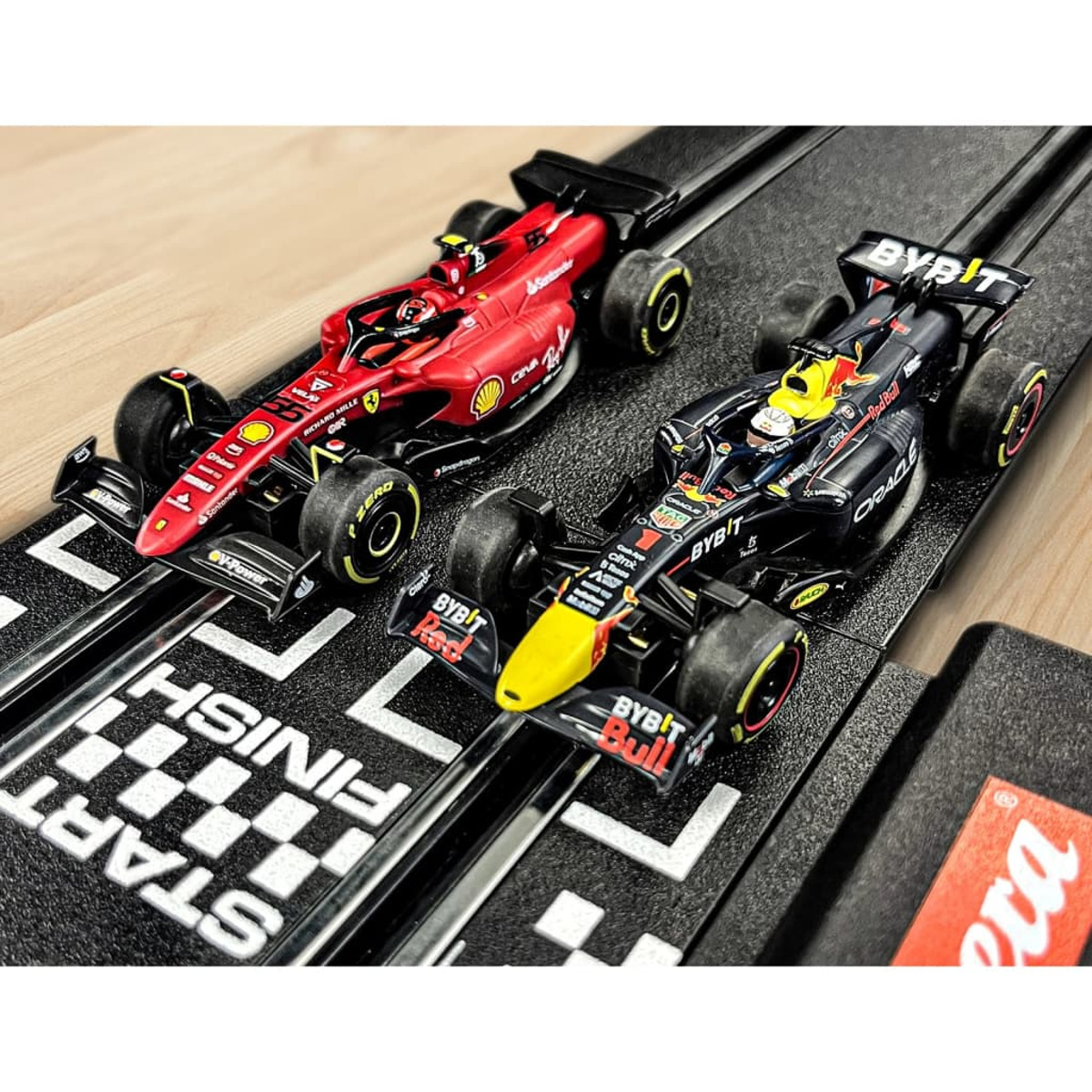 Dwa samochody wyścigowe na torze, jeden czerwony i jeden czarny. Tor ma linię startu i mety.