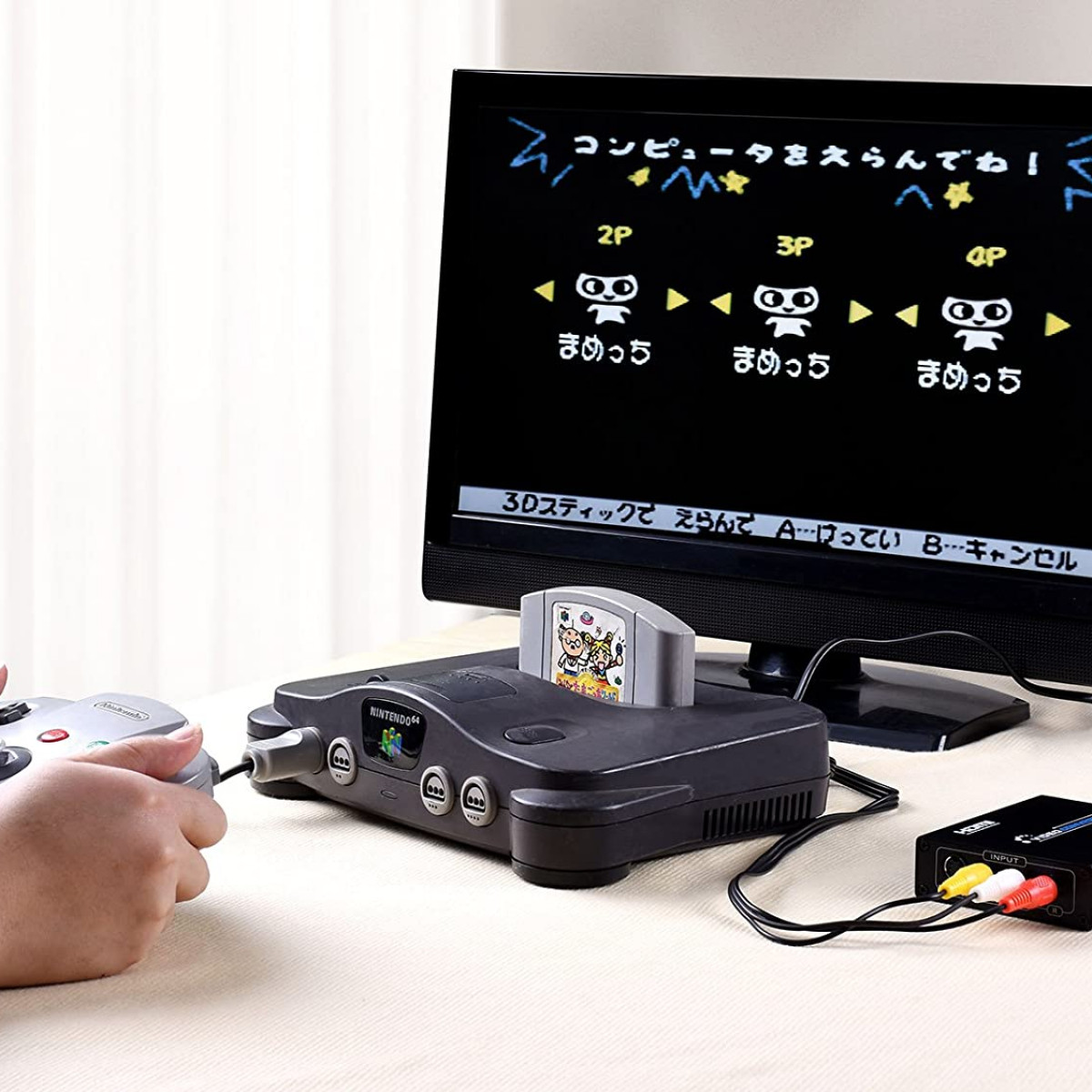 Osoba grająca na retro Nintendo 64 z konsolą i ekranem w tle.