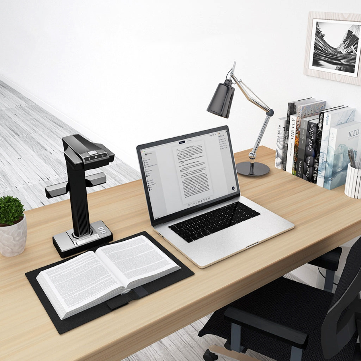 Schreibtisch mit Laptop, Scanner und offenem Buch. Eine Schreibtischlampe und einige Bücher sind ebenfalls vorhanden.