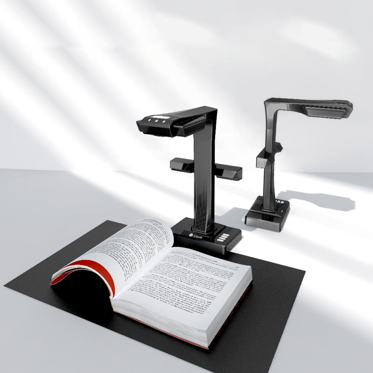 Zwei schwarze Dokumentenscanner und ein offenes Buch auf einer schwarzen Matte. Sonnendurchfluteter Hintergrund.