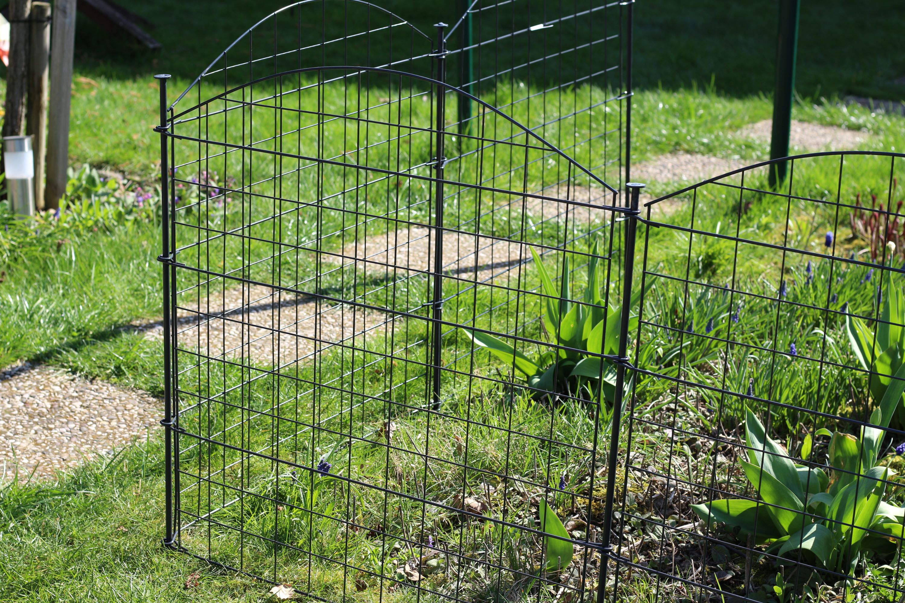 Ein schwarzer Metall-Gartenzaun schlängelt sich durch einen grasbewachsenen Garten.