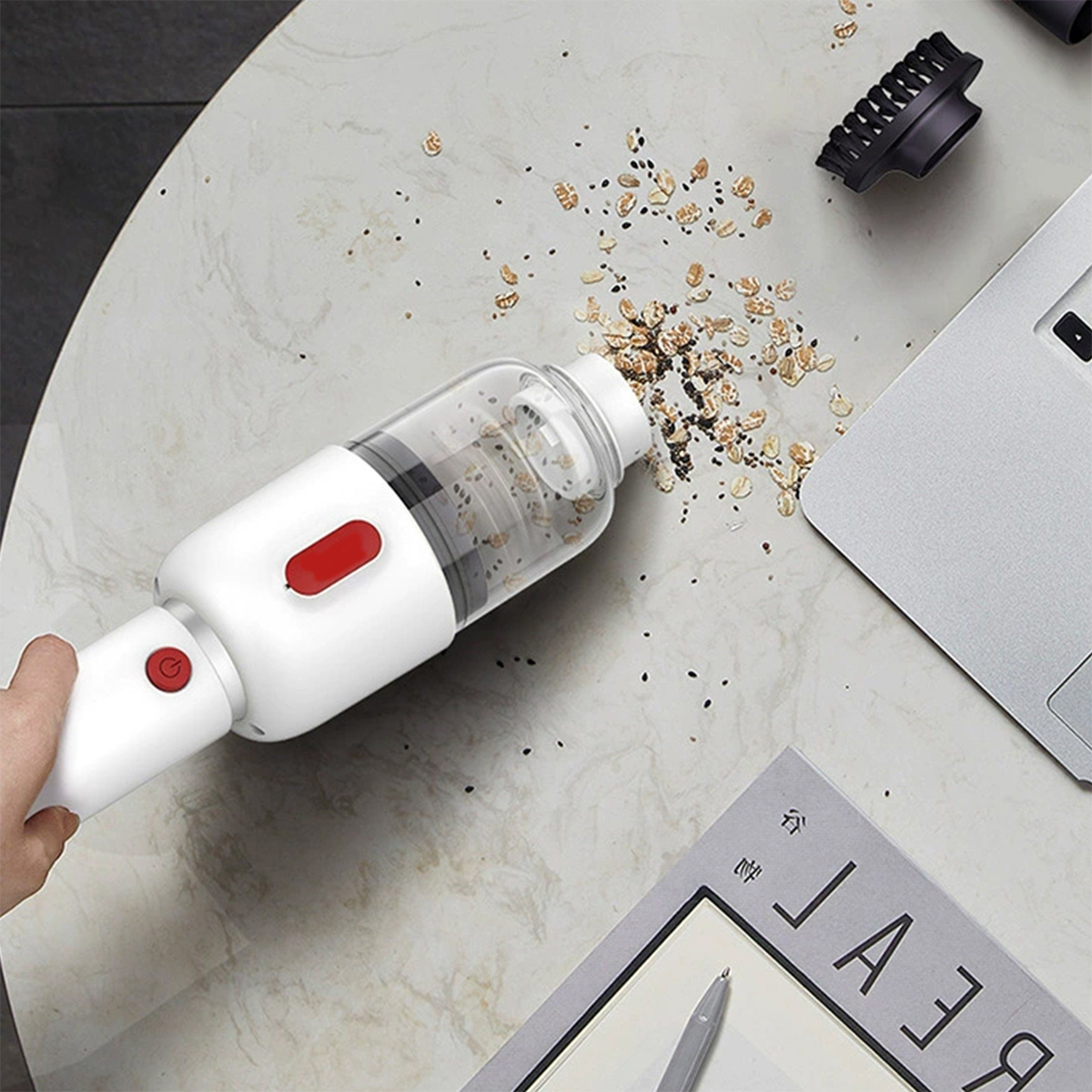 Biały odkurzacz czyszczący ziarna na marmurowym stole, z laptopem i papierem.