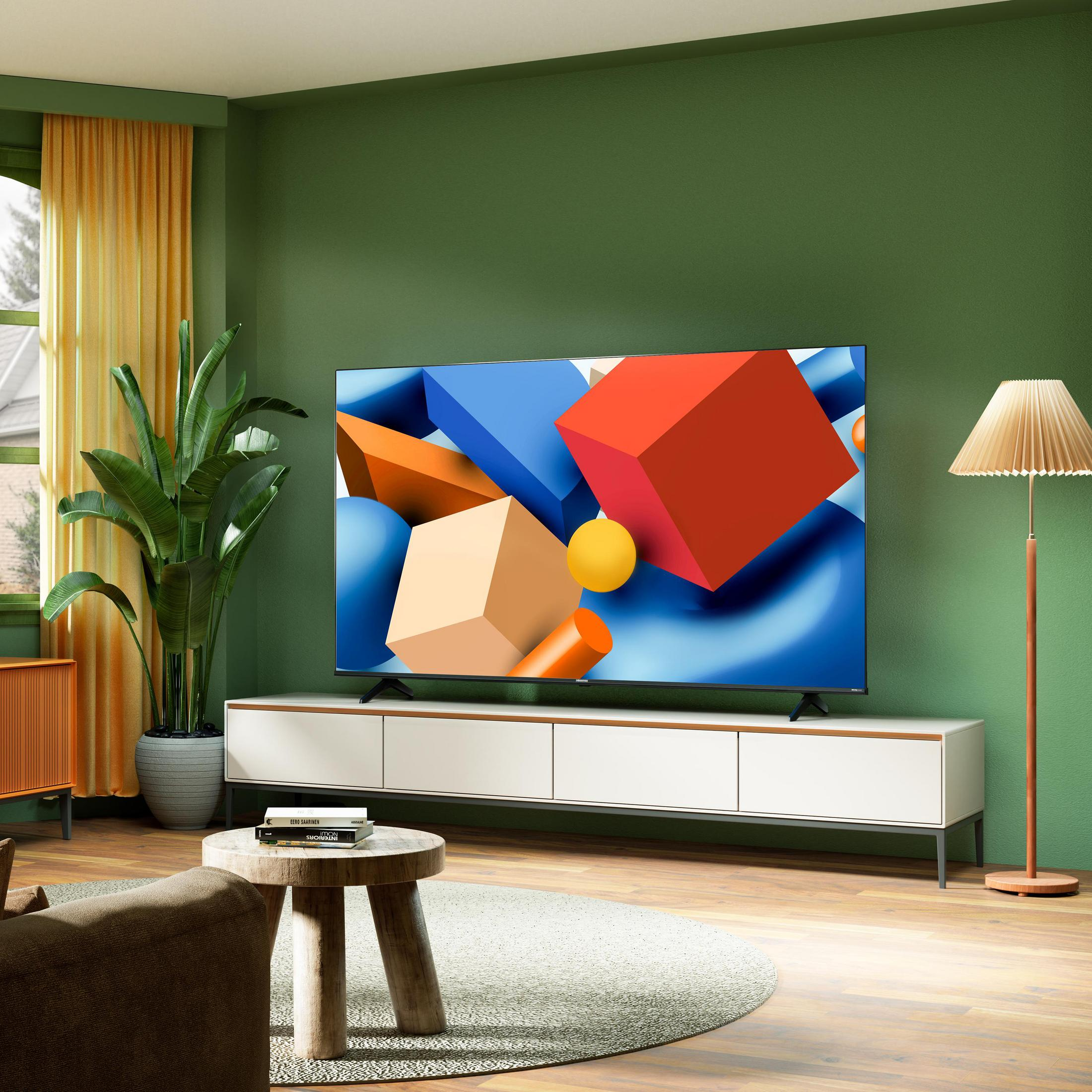 Soggiorno con parete verde, TV, divano, piante e tappeto rotondo.