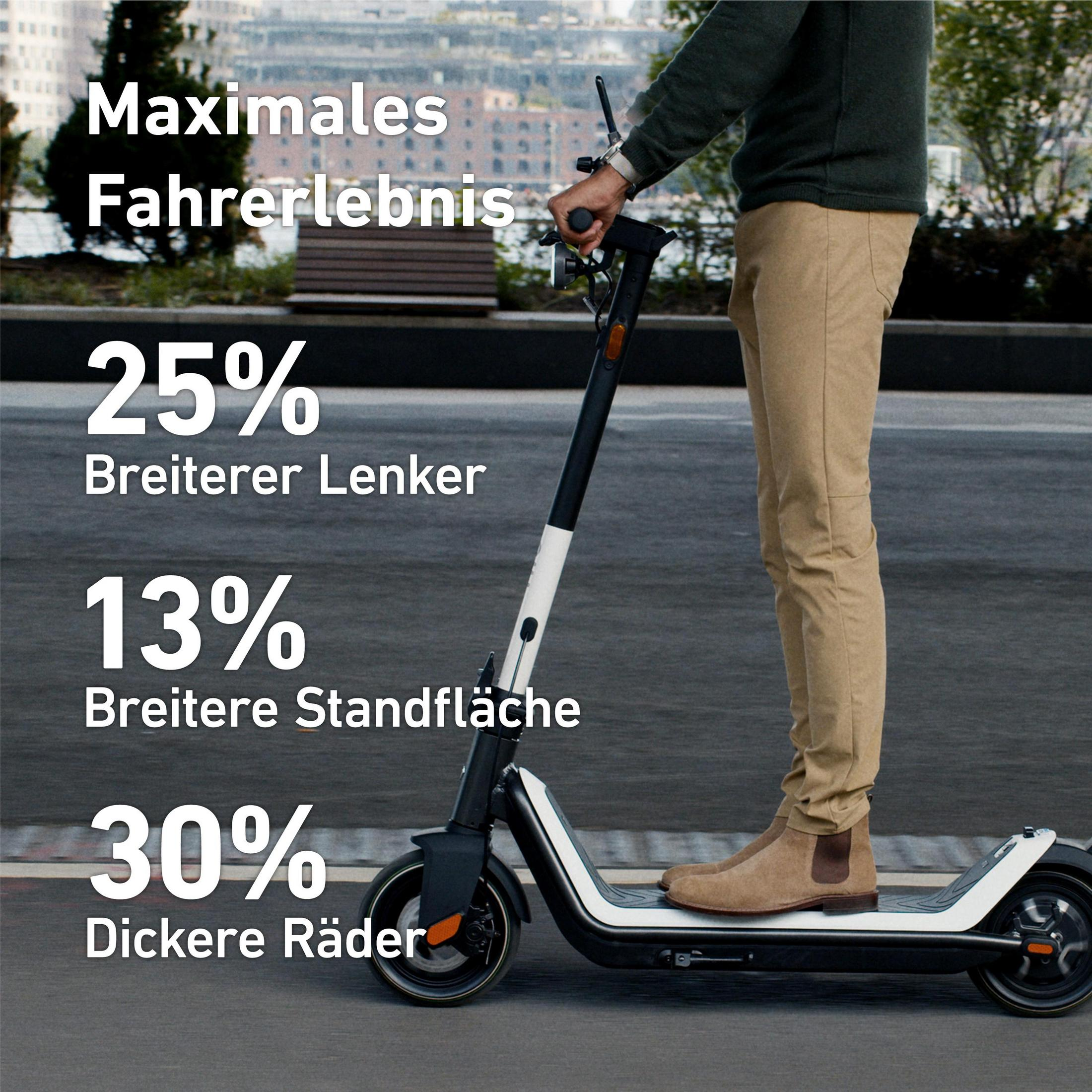Eine Person auf einem Roller. Text wirbt für breitere Lenker, ein breiteres Trittbrett und dickere Räder. Draußen.