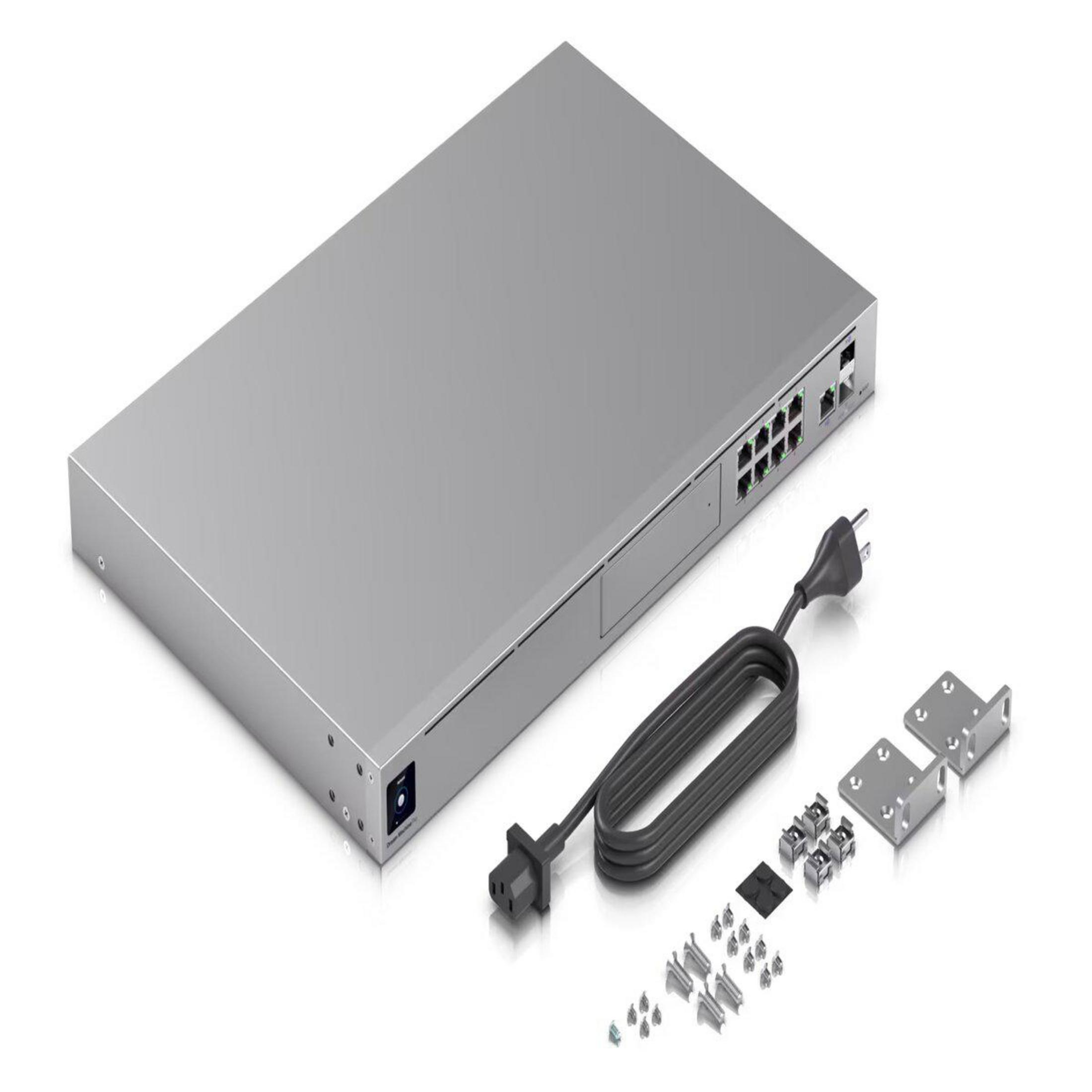 Srebrny przełącznik sieciowy z portami, przewodem zasilającym i osprzętem montażowym na białej powierzchni.