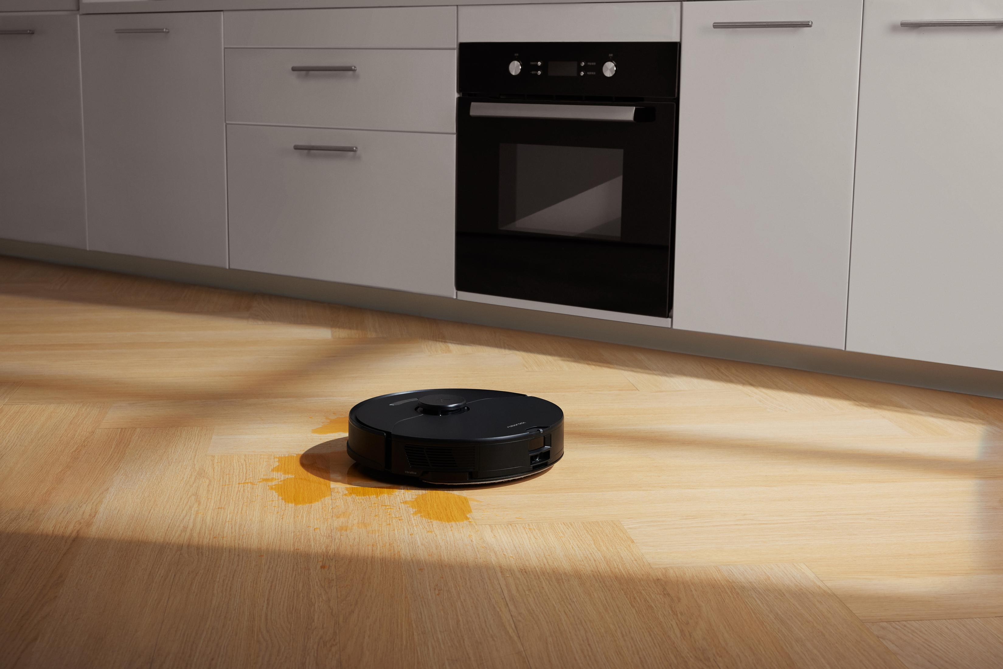 Czarny odkurzacz automatyczny na drewnianej podłodze z plamami wody.