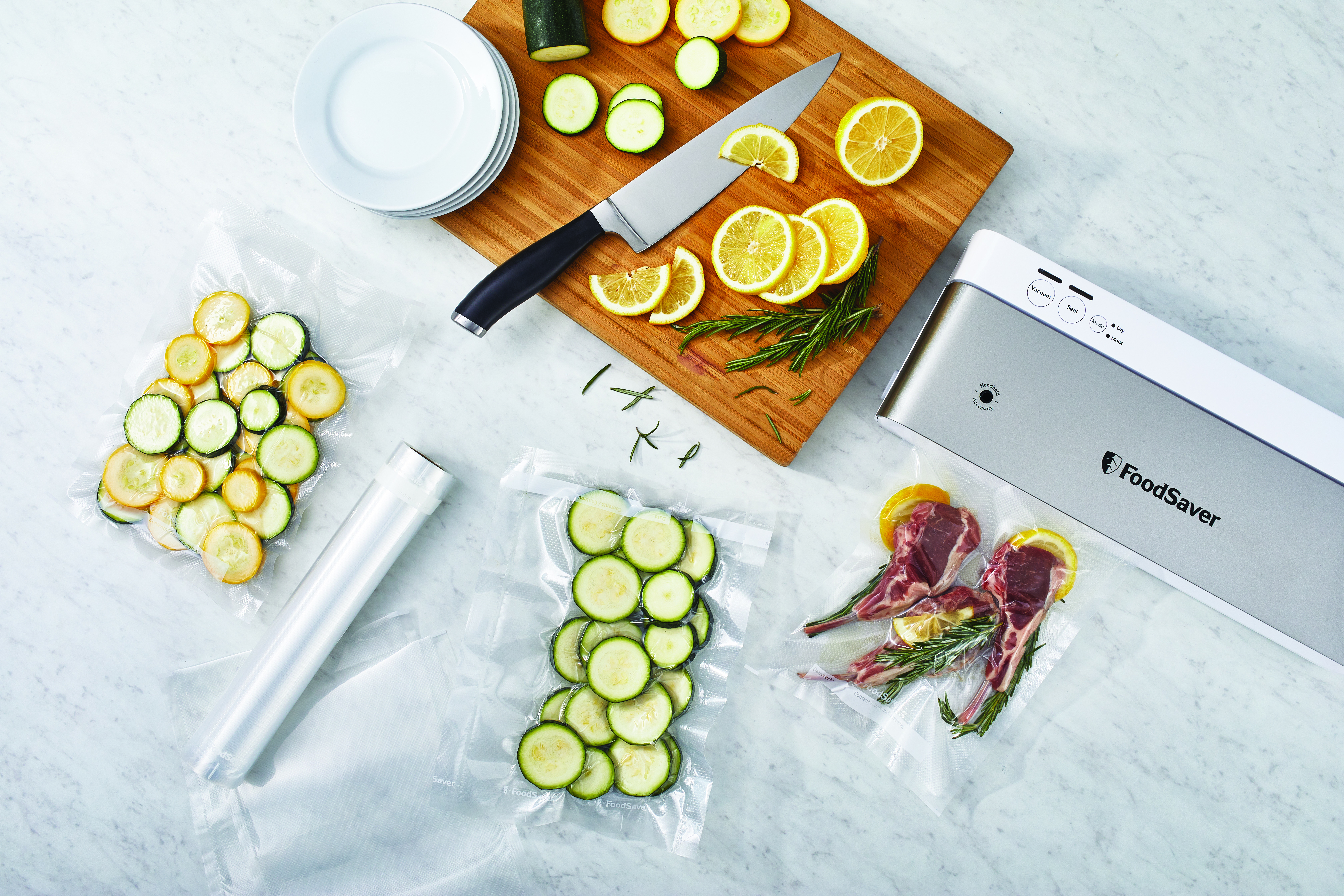 FoodSaver z workami próżniowymi z plastrami cukinii, plasterkami cytryny i ziołami na marmurowej powierzchni.