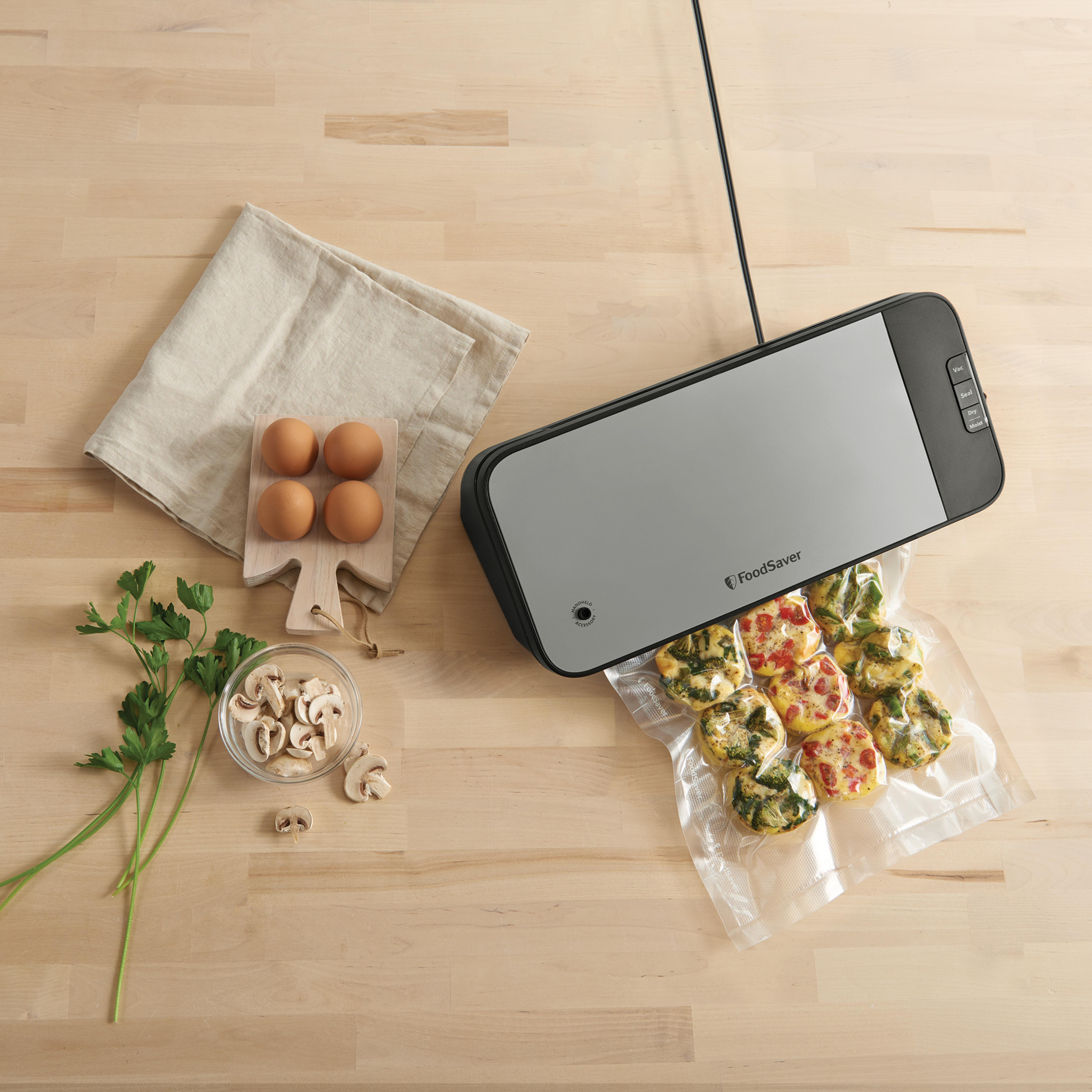 FoodSaver-Maschine, die Lebensmittel vakuumversiegelt. Eier, Petersilie, Pilze und gekochte Speisen in Plastiktüten.