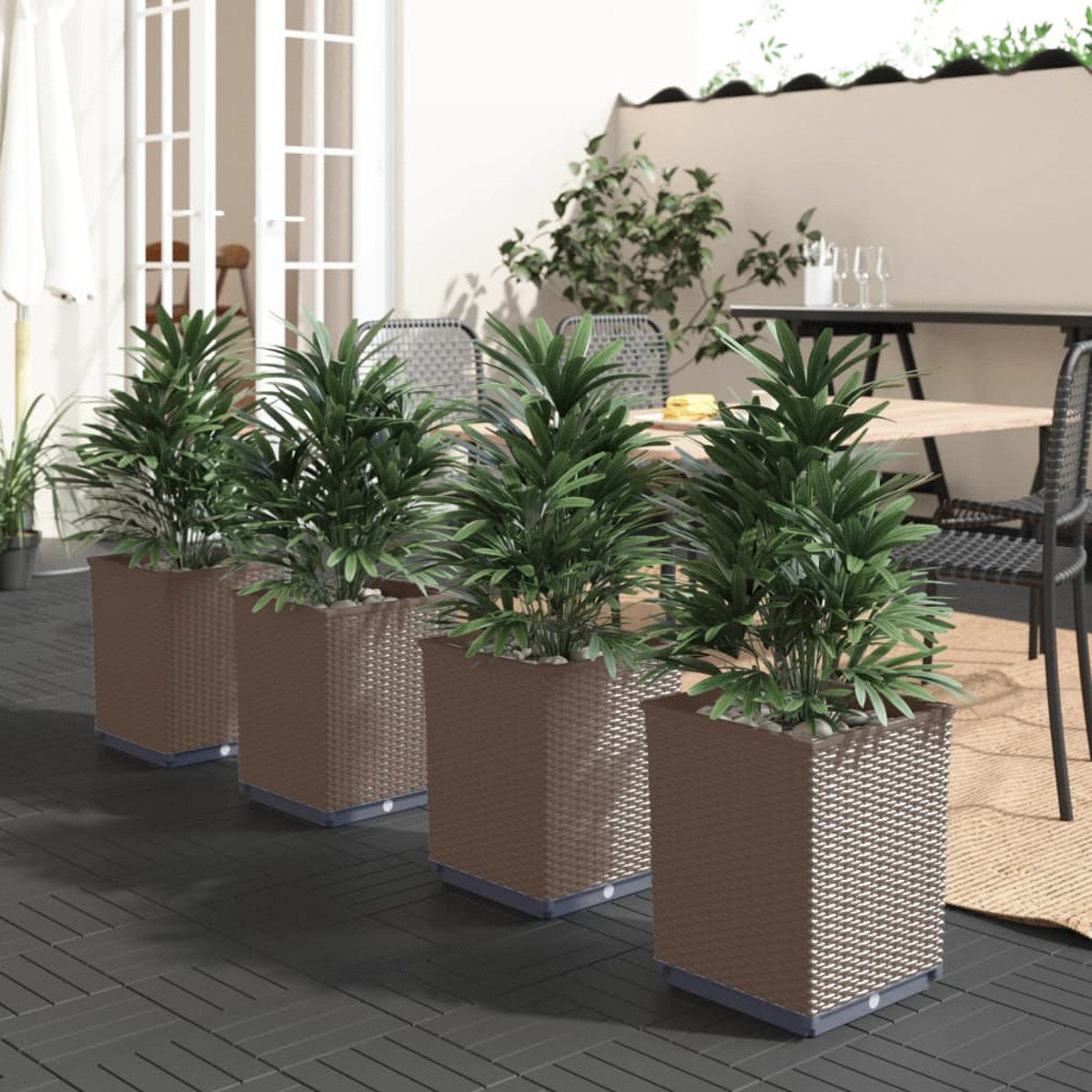 Vier quadratische Pflanzgefäße mit Pflanzen auf einer Terrasse. Hintergrund: Tisch, Stühle, Außenbereich.