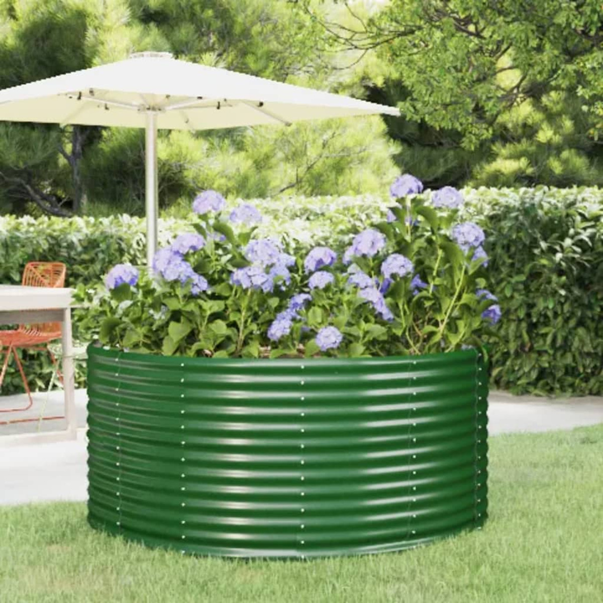 Grünes Metall-Gartenbeet, gefüllt mit blauen Blumen, unter einem Sonnenschirm auf Gras. Hintergrund Bäume.