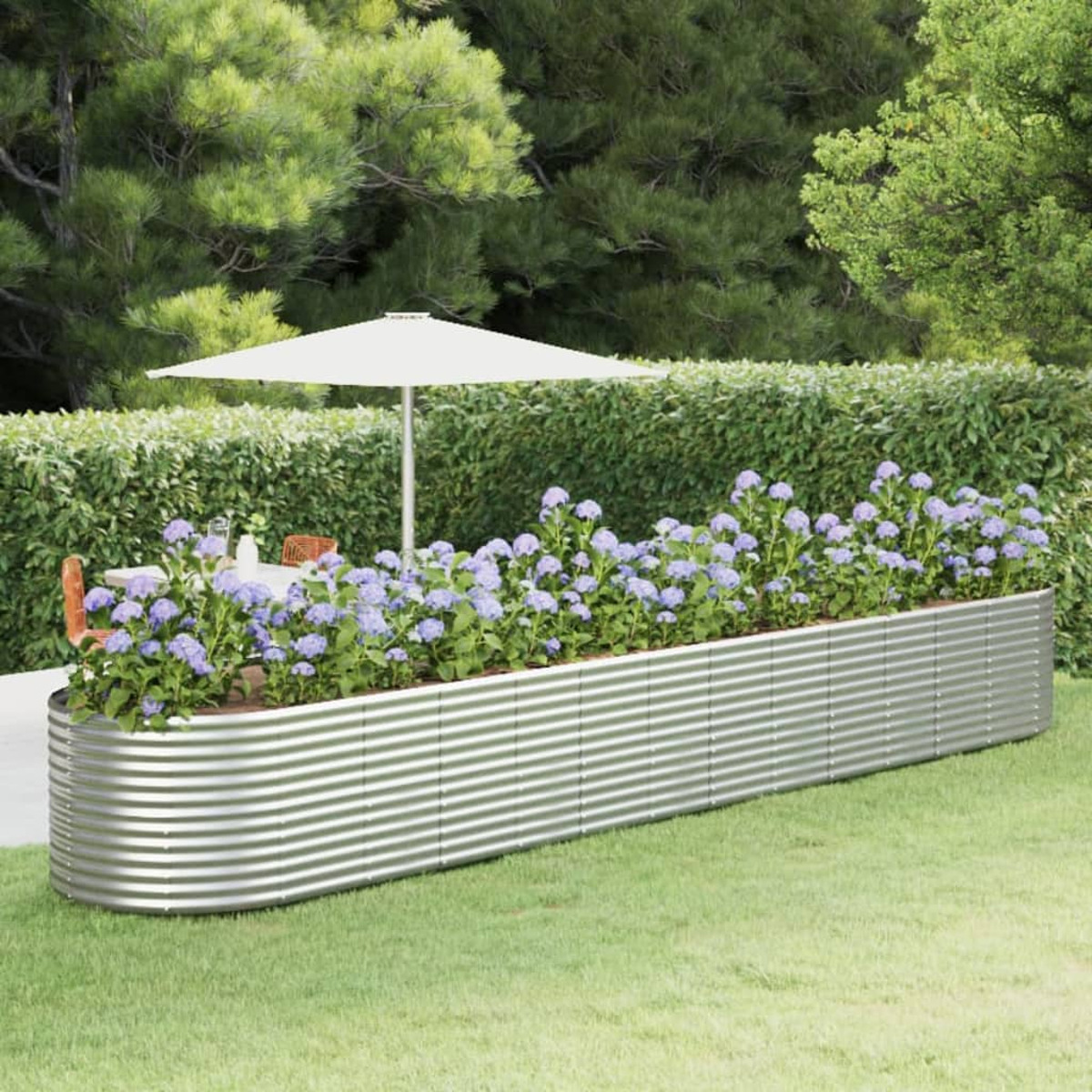Ein langer, silberfarbener Metallpflanzer mit Blumen. Im Hintergrund eine Terrassengarnitur.