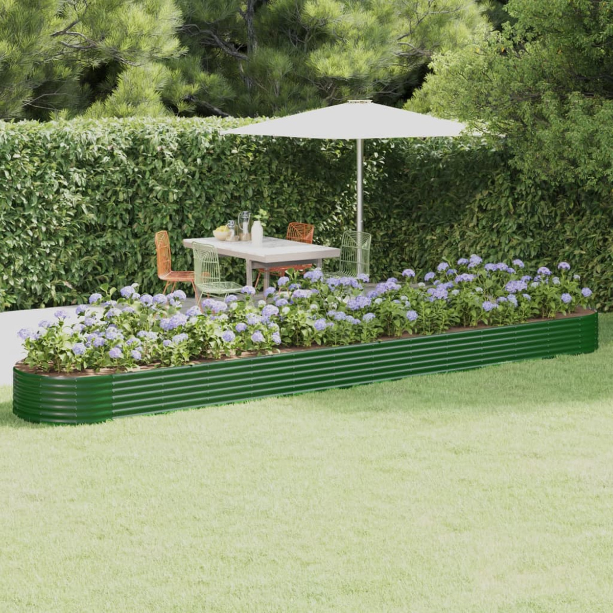 Grüner Metallpflanzer mit lila Blumen. Weißer Sonnenschirm, Tisch, Stühle und Hecke im Hintergrund; Gras im Vordergrund.