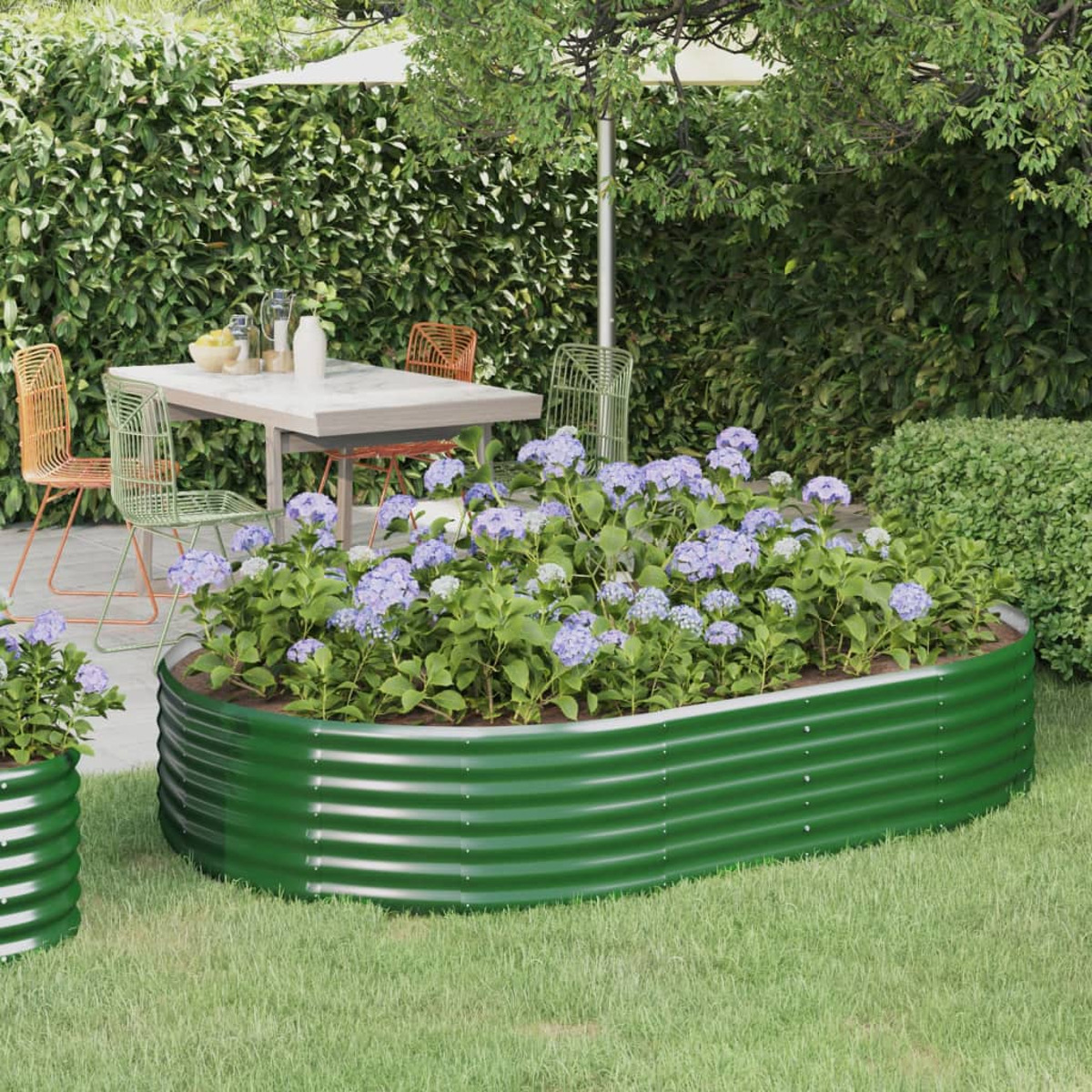 Ein erhöhtes Gartenbeet mit blauen Blumen, einem Tisch und Stühlen in einem Garten.