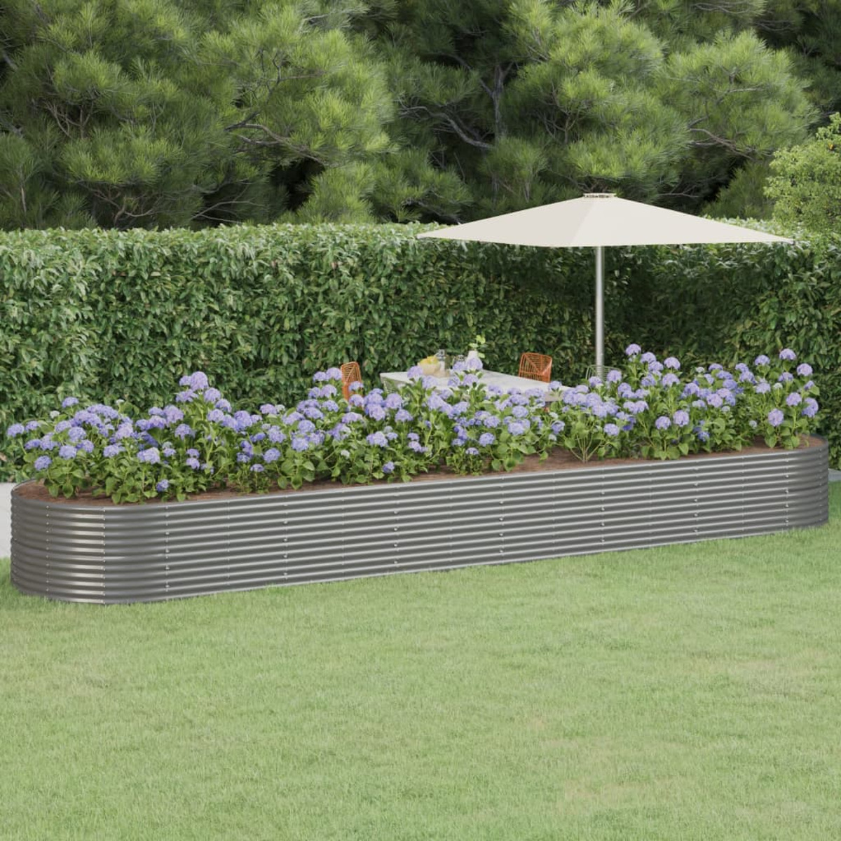 Ein langes, wellblechförmiges Hochbeet mit Blumen und Grün, mit einem Tisch im Hintergrund.