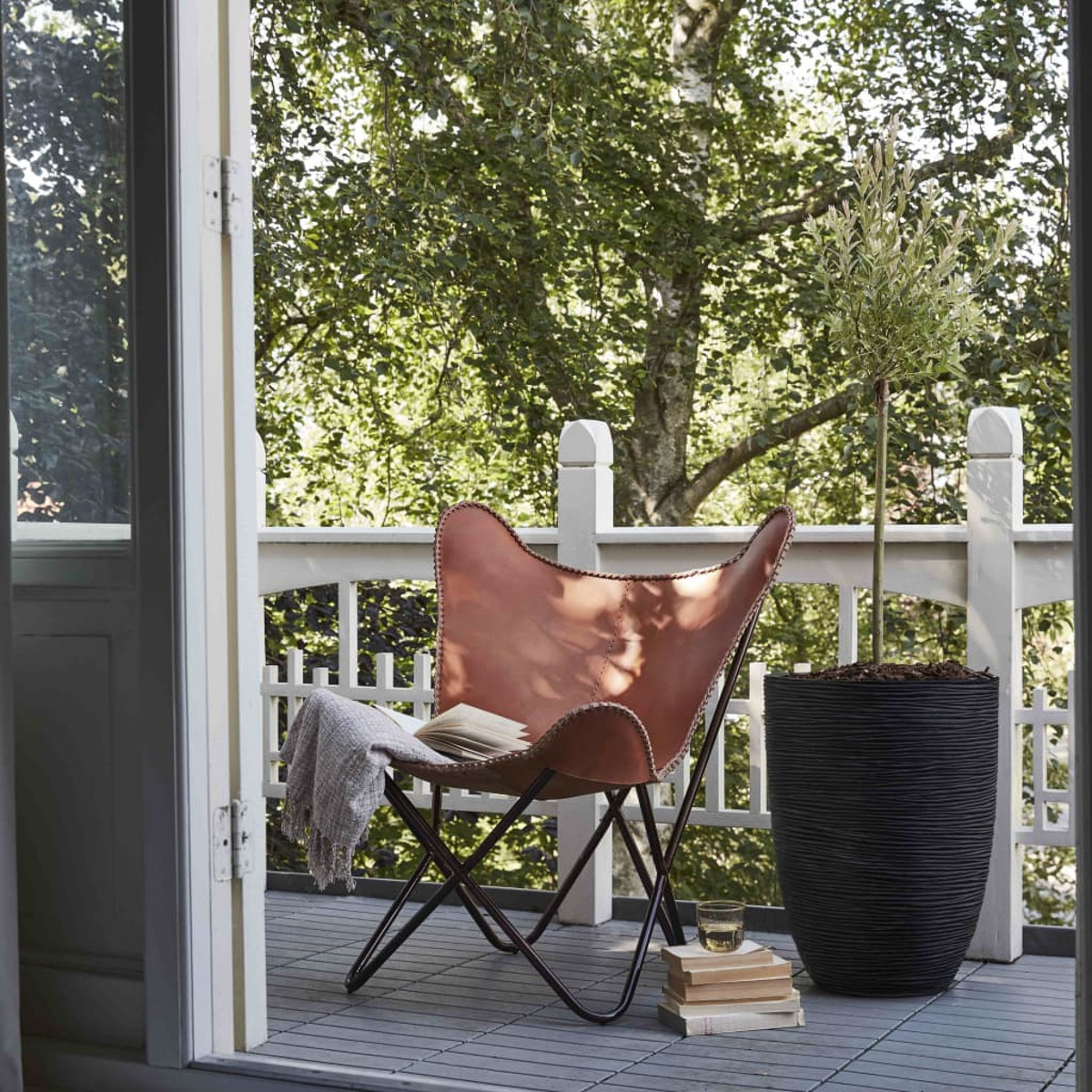 Ein Balkon mit einem Ledersessel, Büchern und einem schwarzen Topf. Bäume im Hintergrund.