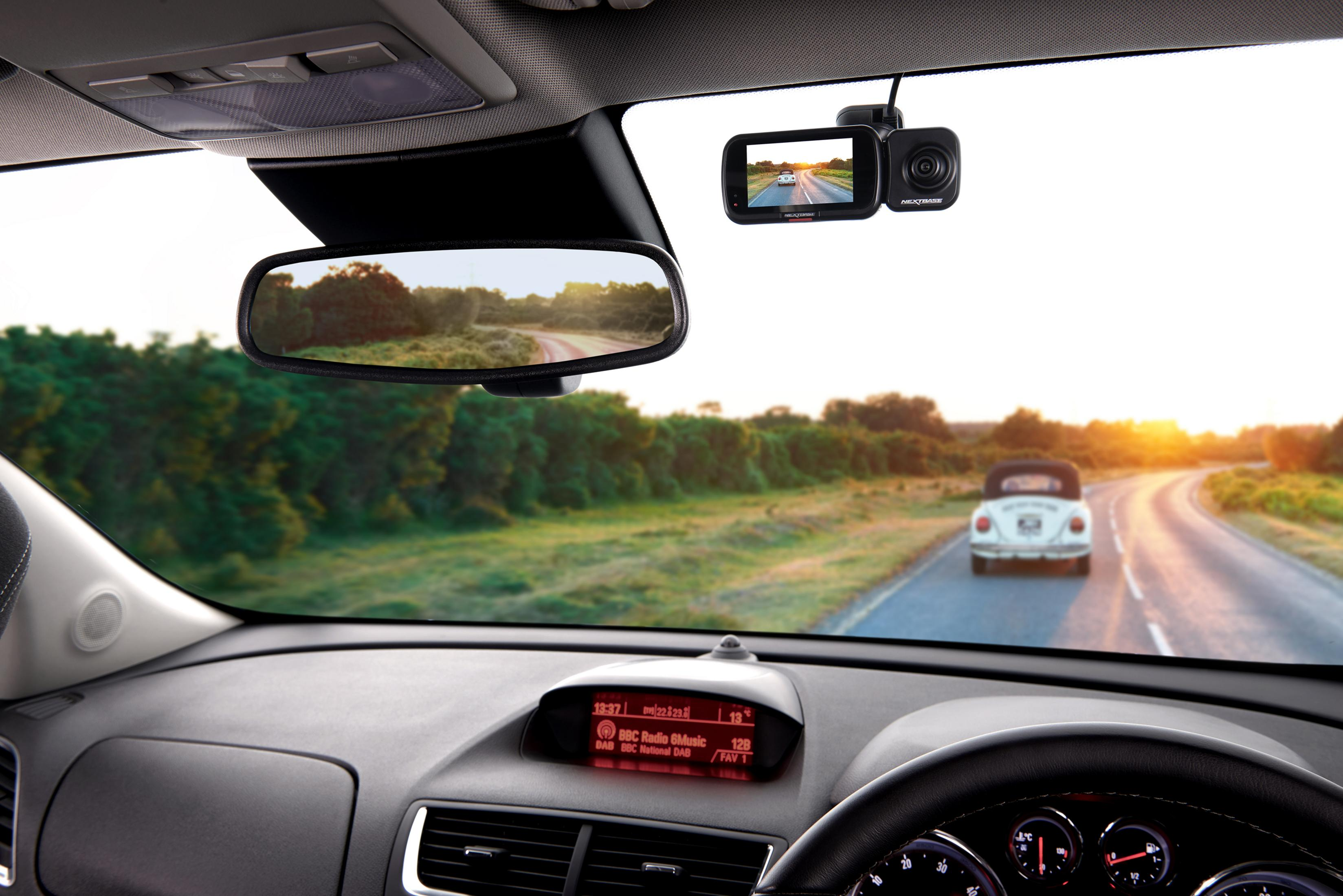 Vista dall'interno di un'auto. Strada di fronte, specchietto retrovisore, dashcam e cruscotto visibili.