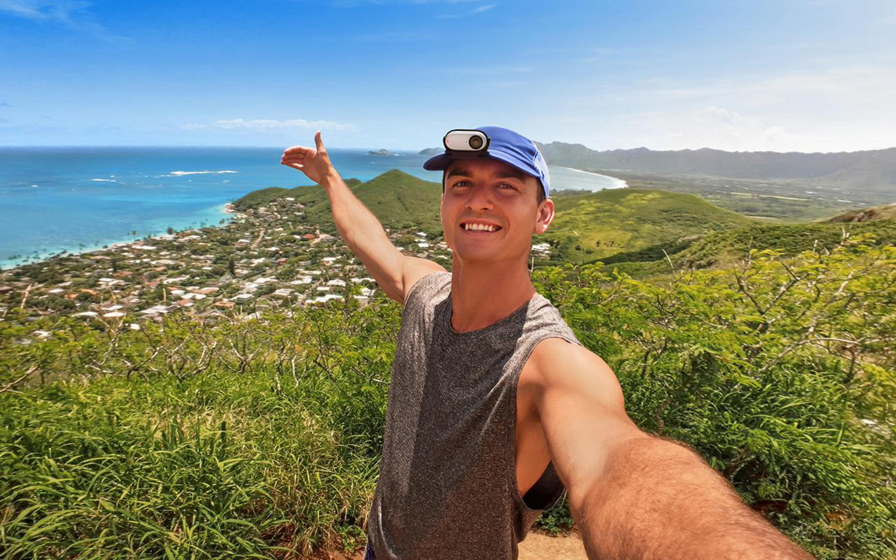 Mężczyzna robiący selfie na wzgórzu z widokiem na ocean i miasto.