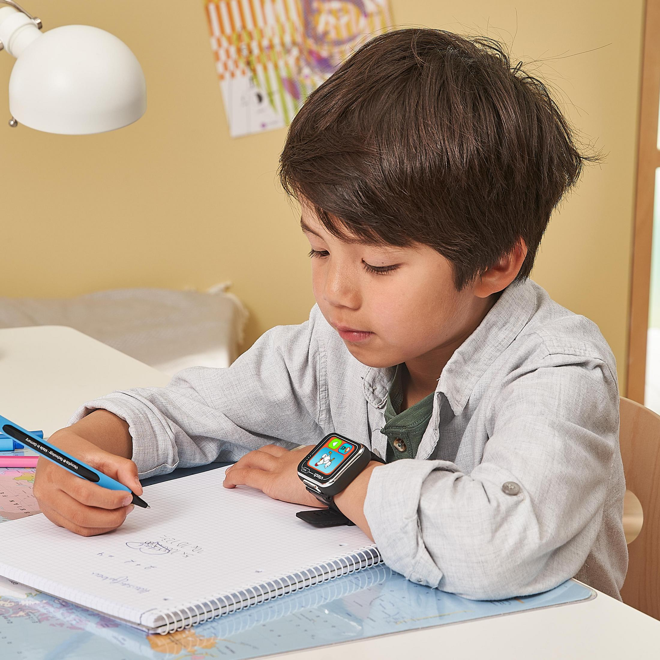 Ein Junge sitzt am Schreibtisch und schreibt in ein Notizbuch. Er trägt eine Smartwatch.