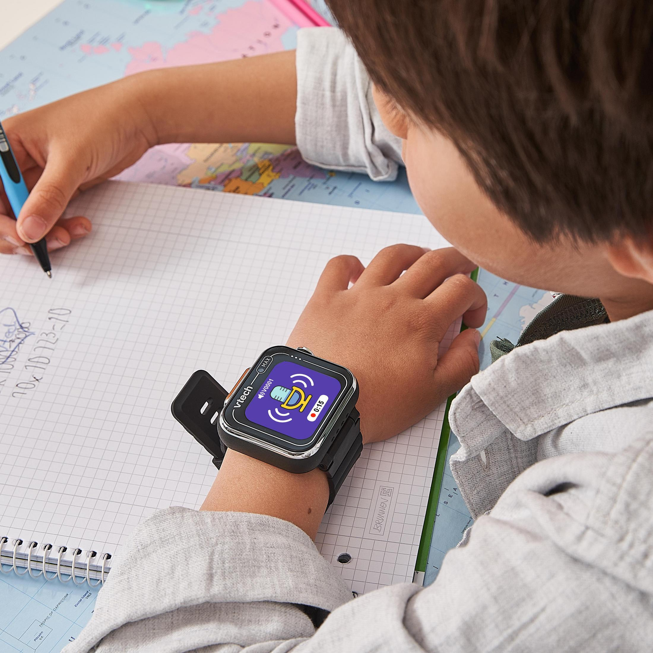 Kind schreibt in Notizbuch mit VTech-Smartwatch am Handgelenk auf Weltkarte.
