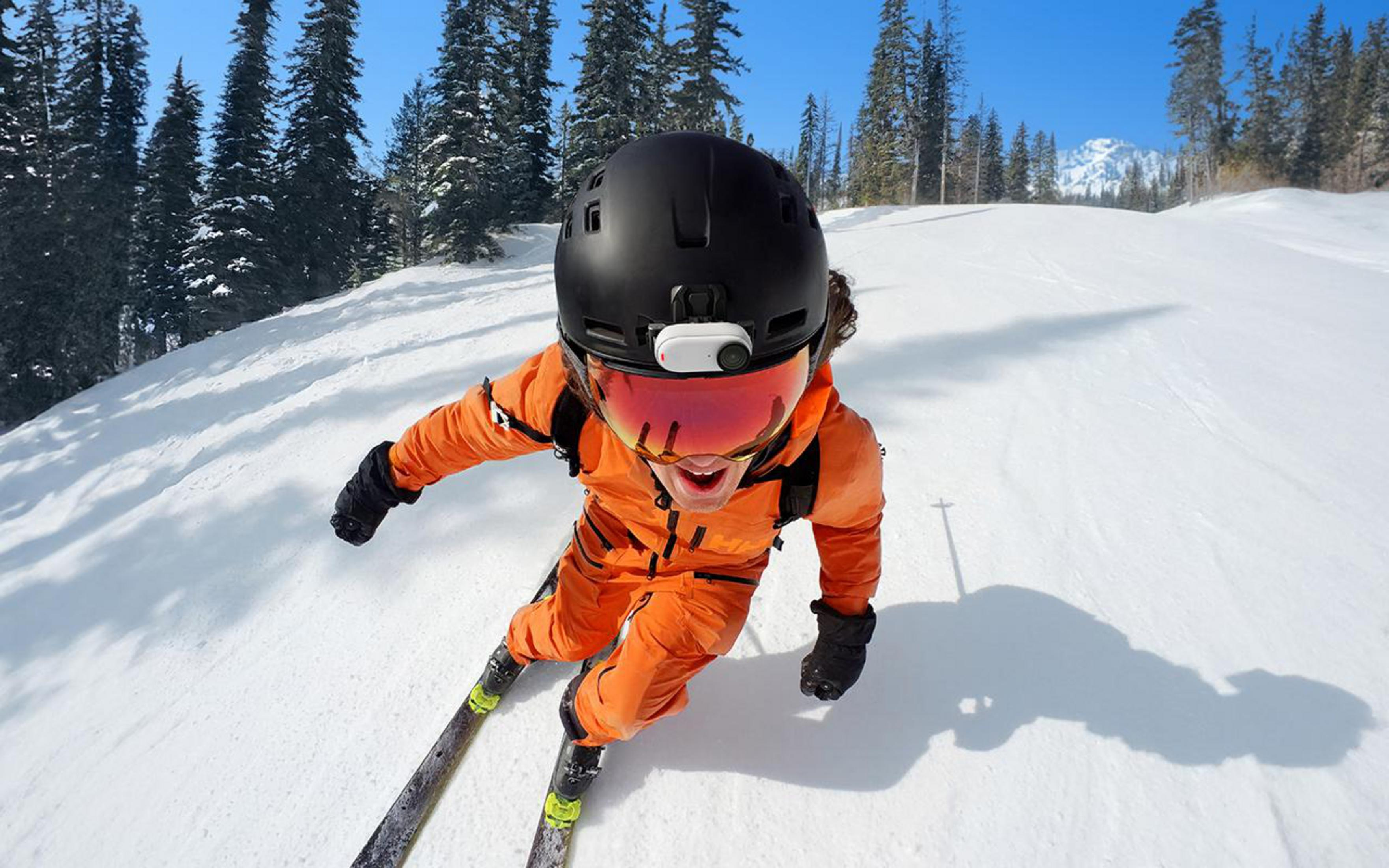 Skier in orange suit, black helmet with a camera, skiing on snow.
