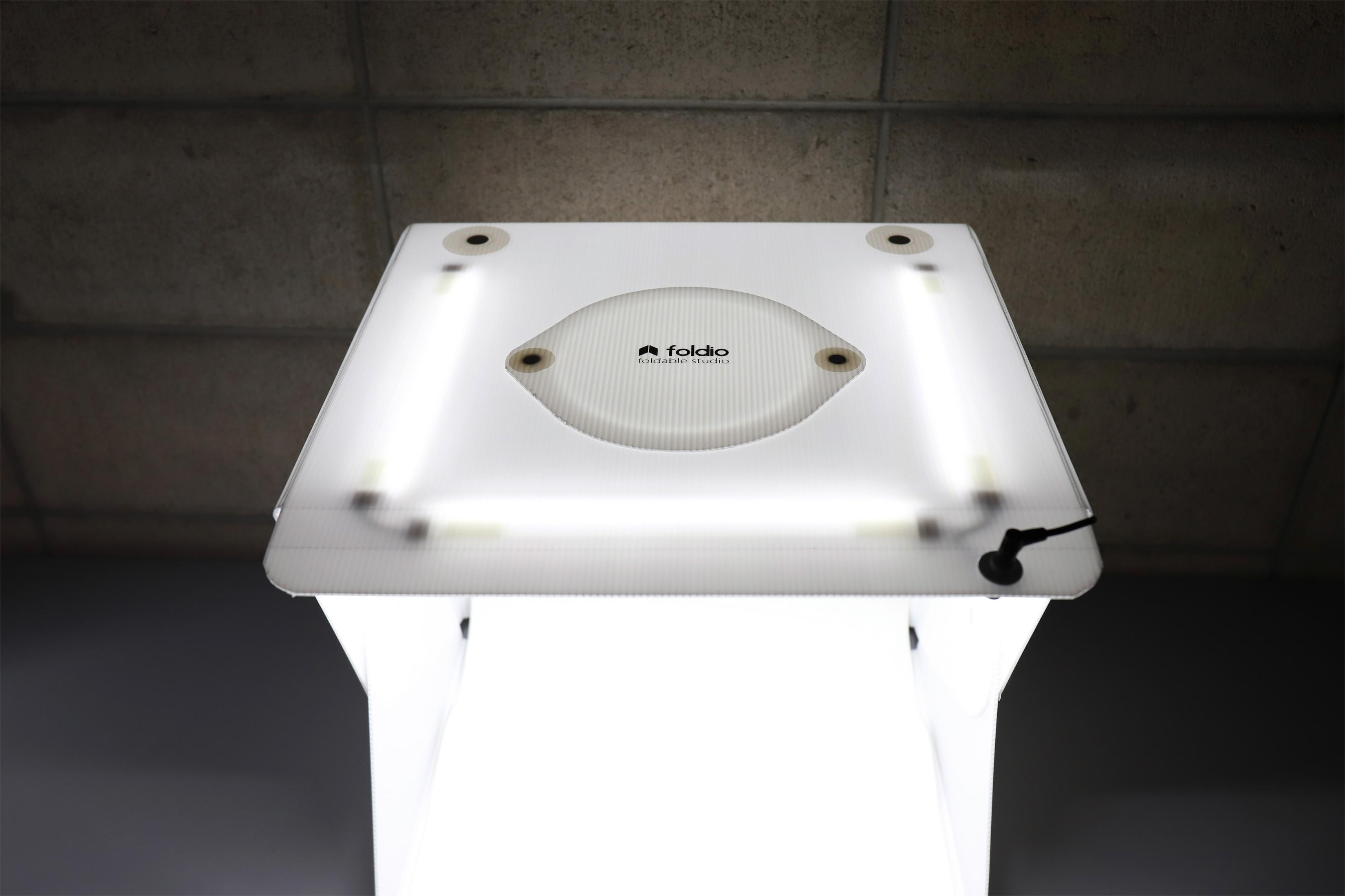 Weisse Lichtbox mit Logo, zwei hellen Leuchtröhren auf grauer Oberfläche.