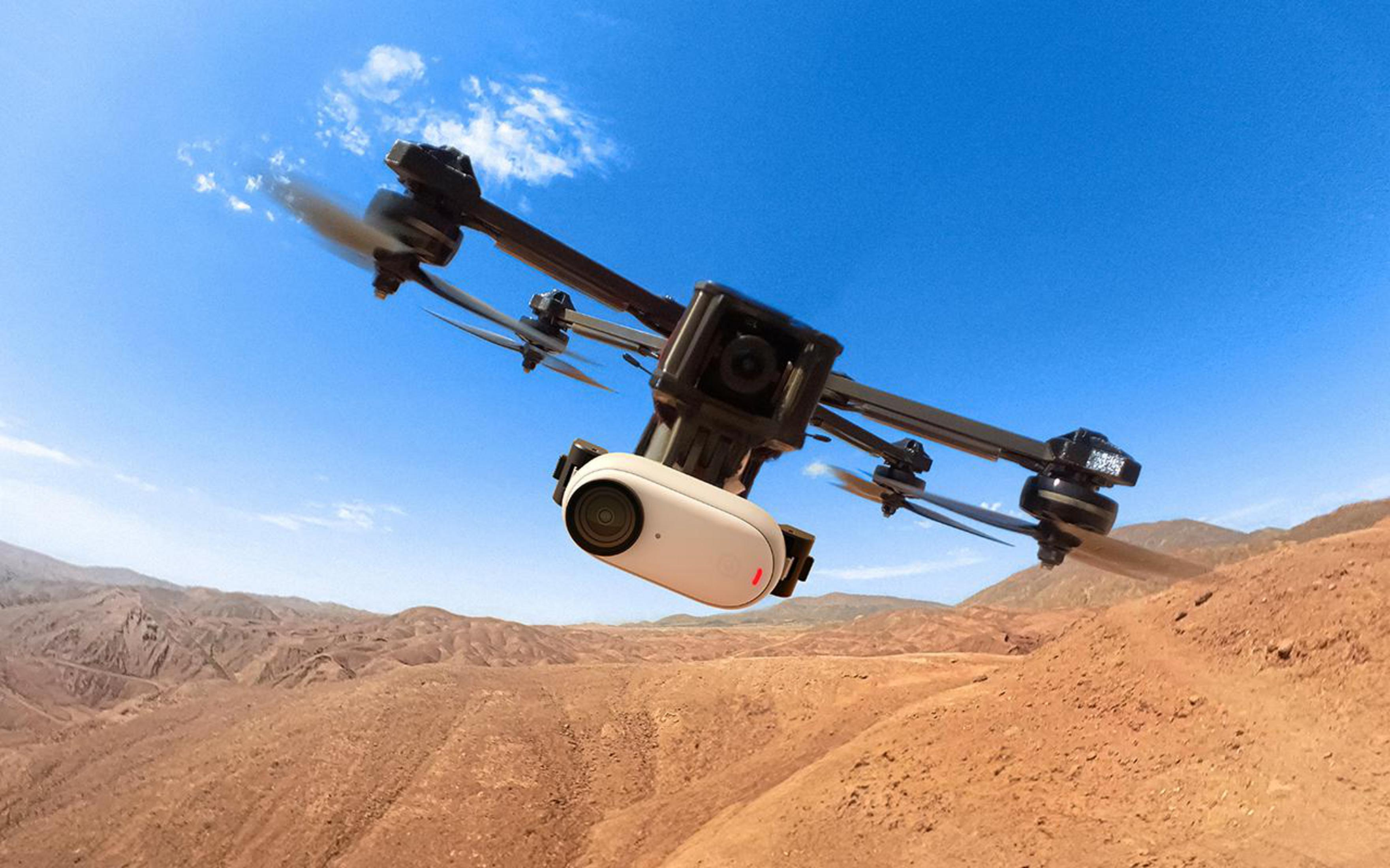 Dron lecący na niebieskim niebie nad pustynnym krajobrazem. Dron ma dołączoną kamerę.