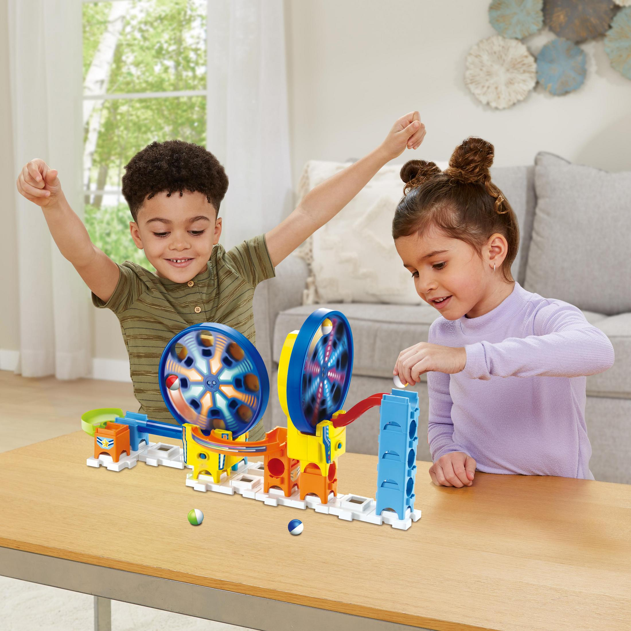 Zwei Kinder spielen mit einem Murmelbahn-Spielzeug, ein Kind hebt aufgeregt die Arme.