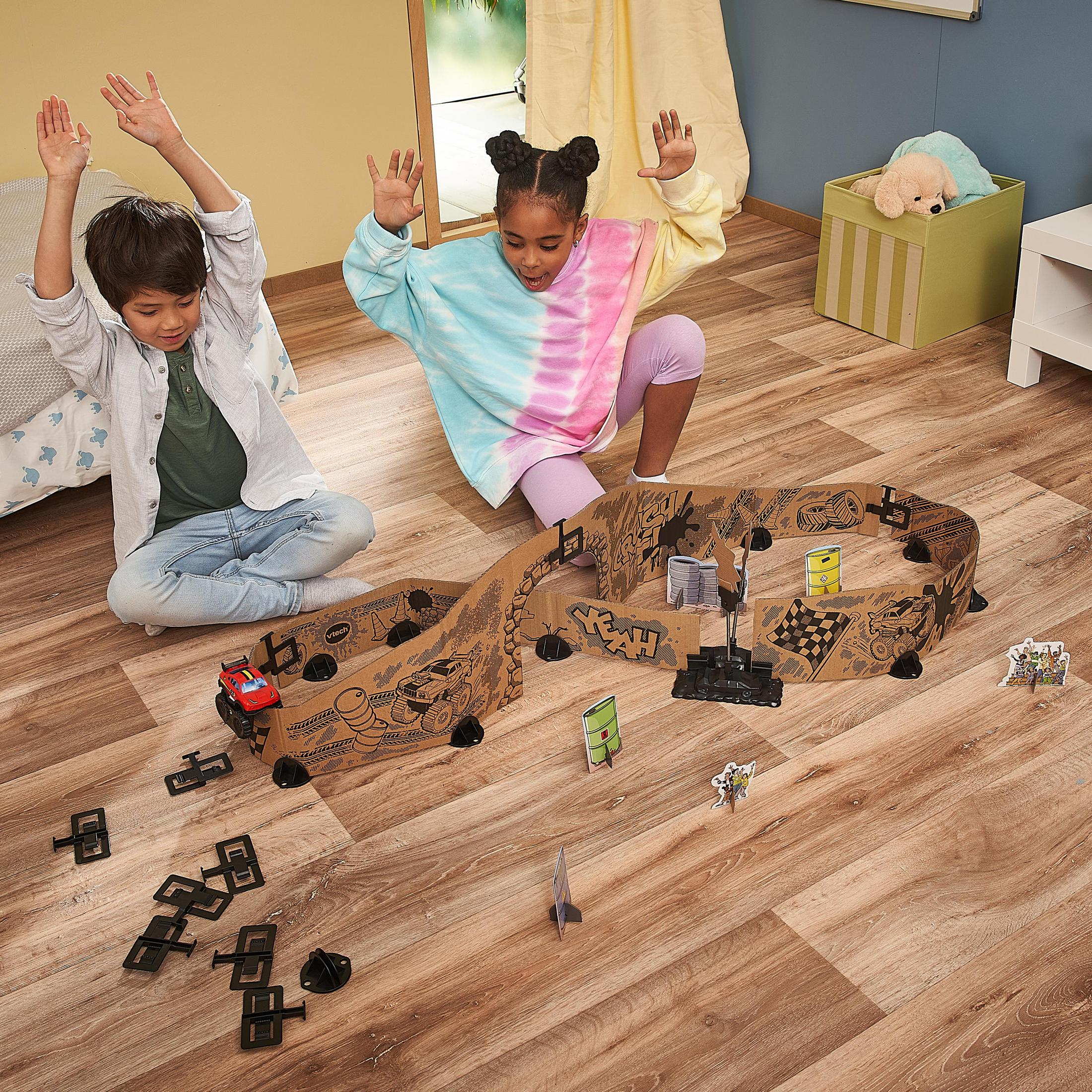 Zwei Kinder spielen mit einer Spielzeug-Rennstrecke. Die Strecke ist braun mit schwarzem Rand.