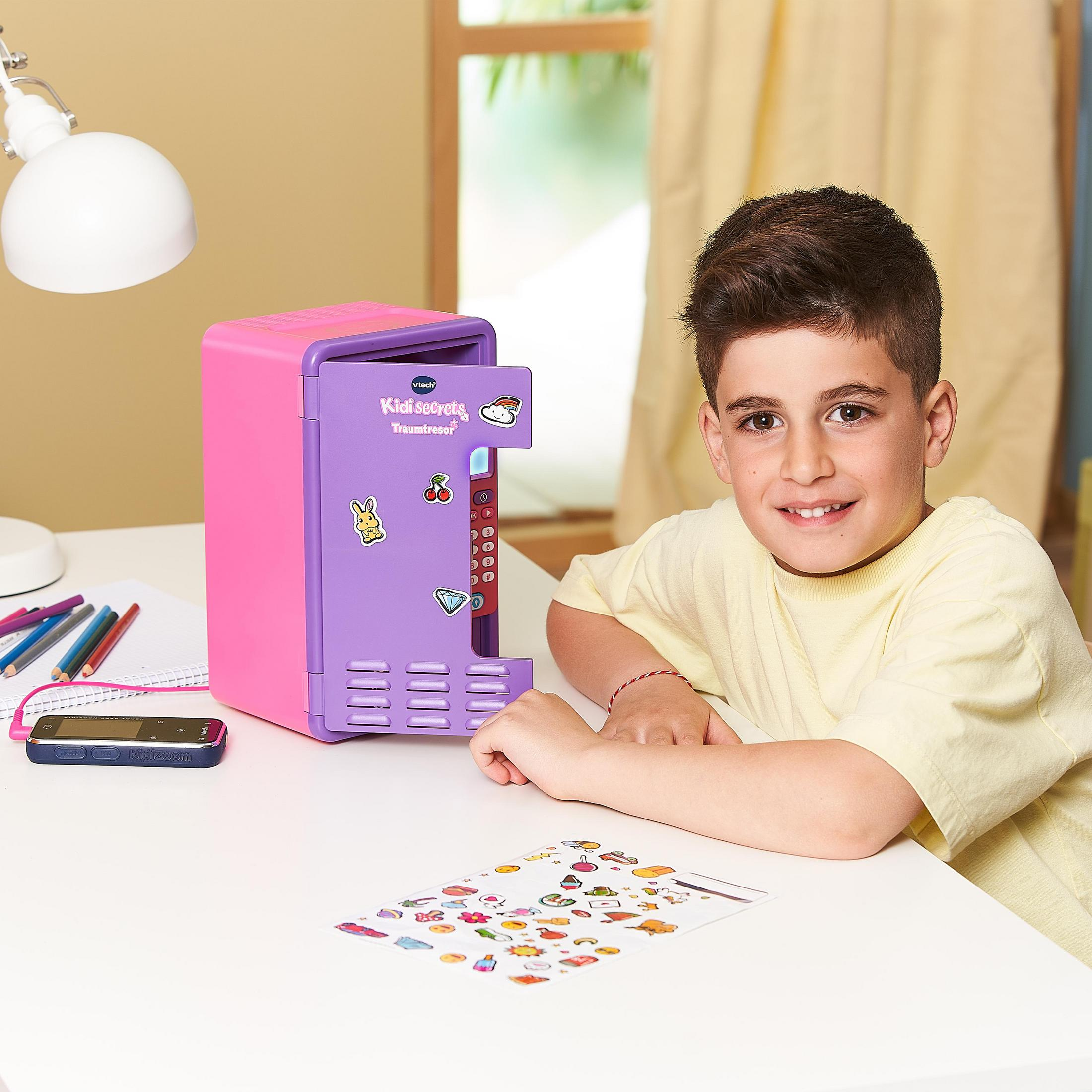 Ein Junge lächelt mit einem pinken Safe. Auf einem weißen Schreibtisch liegen Aufkleber und ein Telefon.