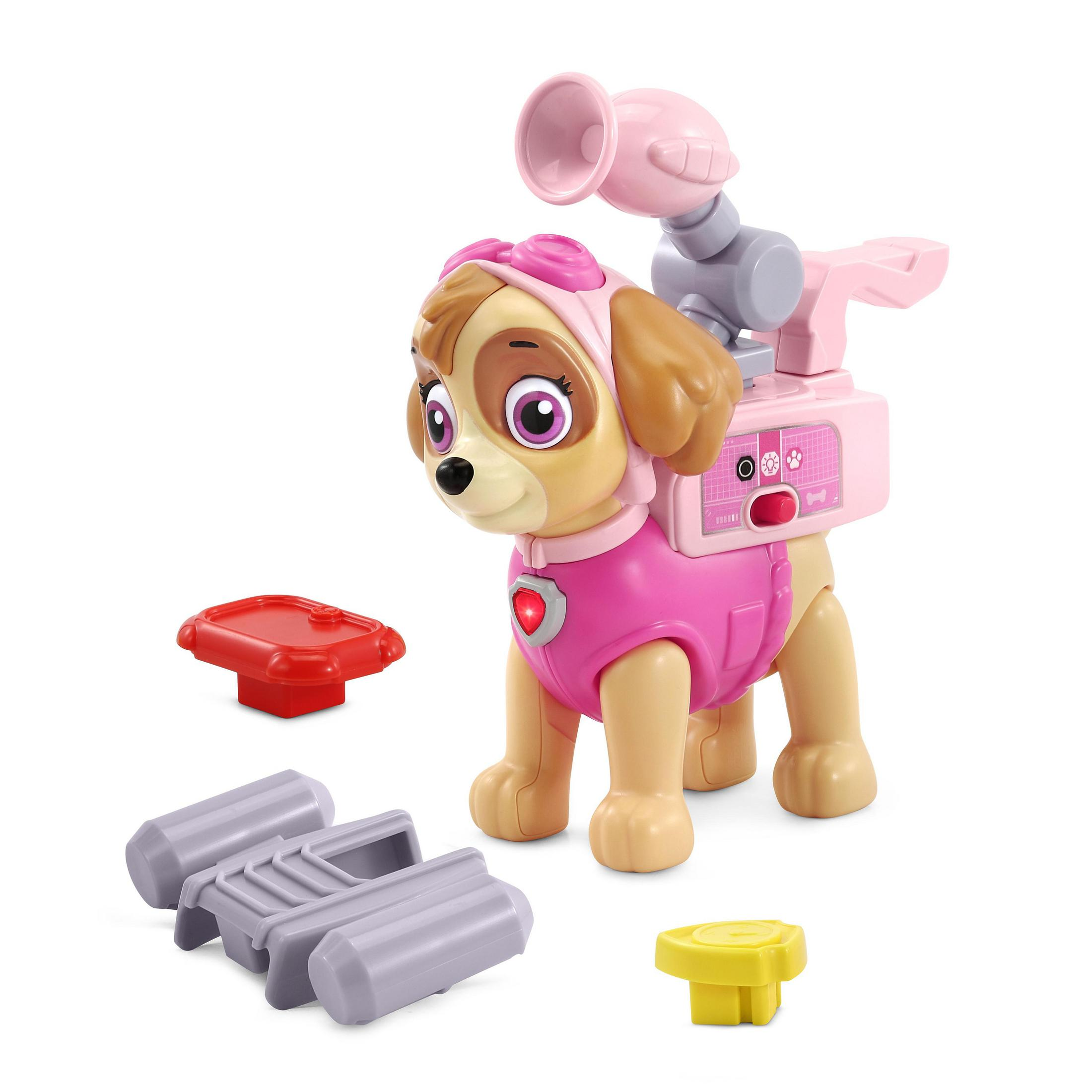 Paw Patrol Skye Spielzeug steht auf weißer Oberfläche, Zubehör in der Nähe. Rosa und Grau dominieren.