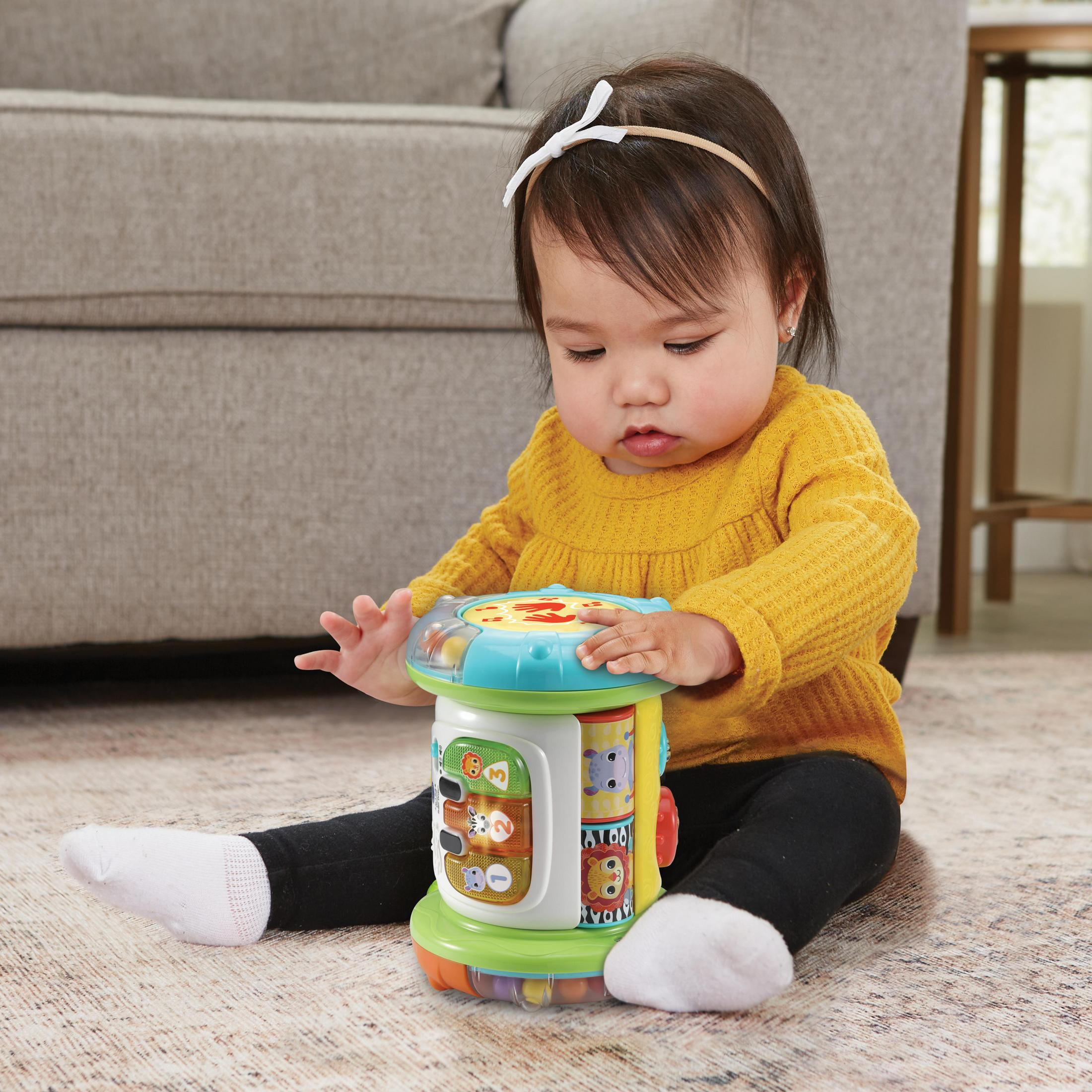 Baby spielt mit buntem Spielzeug, trägt gelbes Oberteil, schwarze Hose und weiße Socken, sitzt auf einem Teppich.