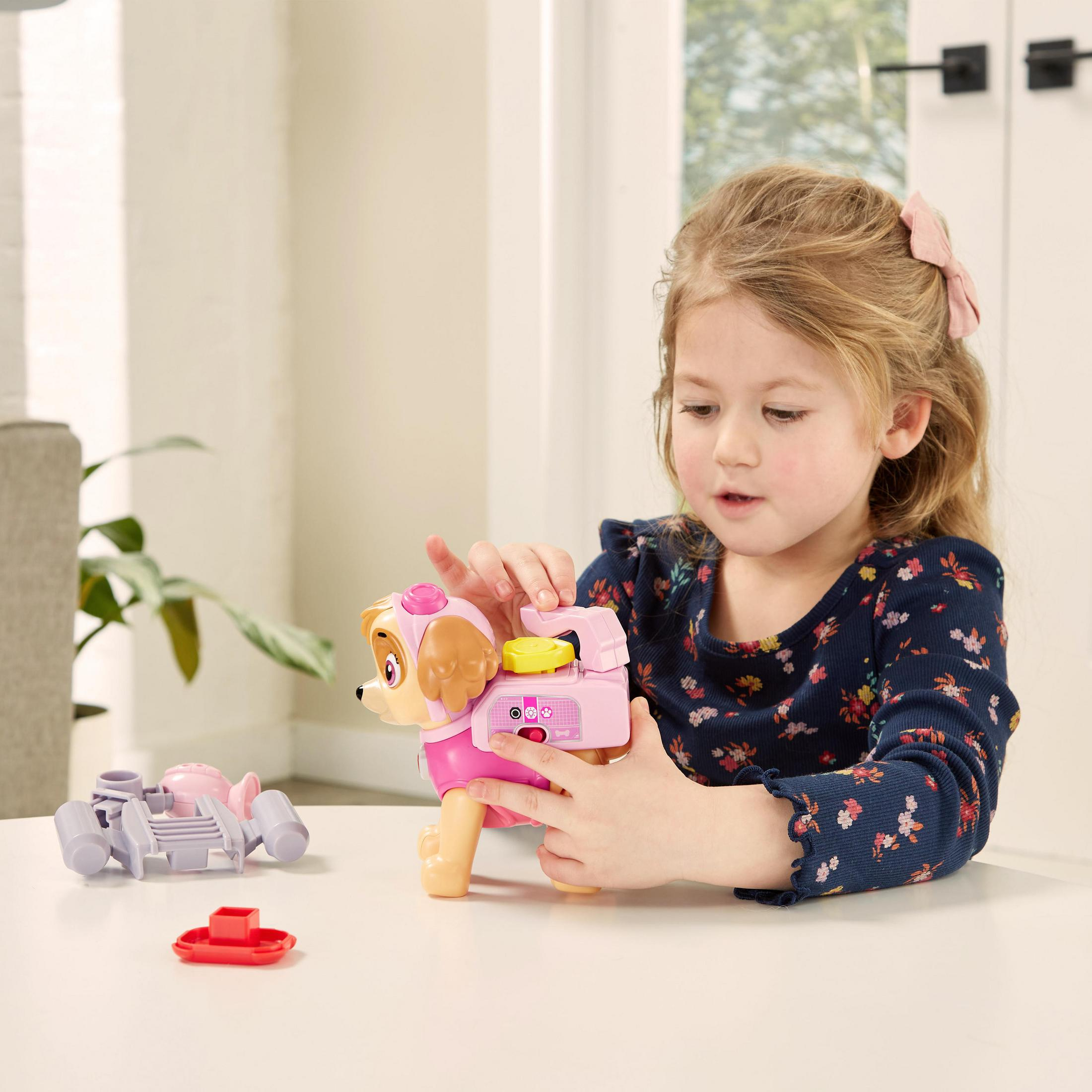 Mädchen spielt mit rosa Spielzeughund, auf weißem Tisch, drinnen.