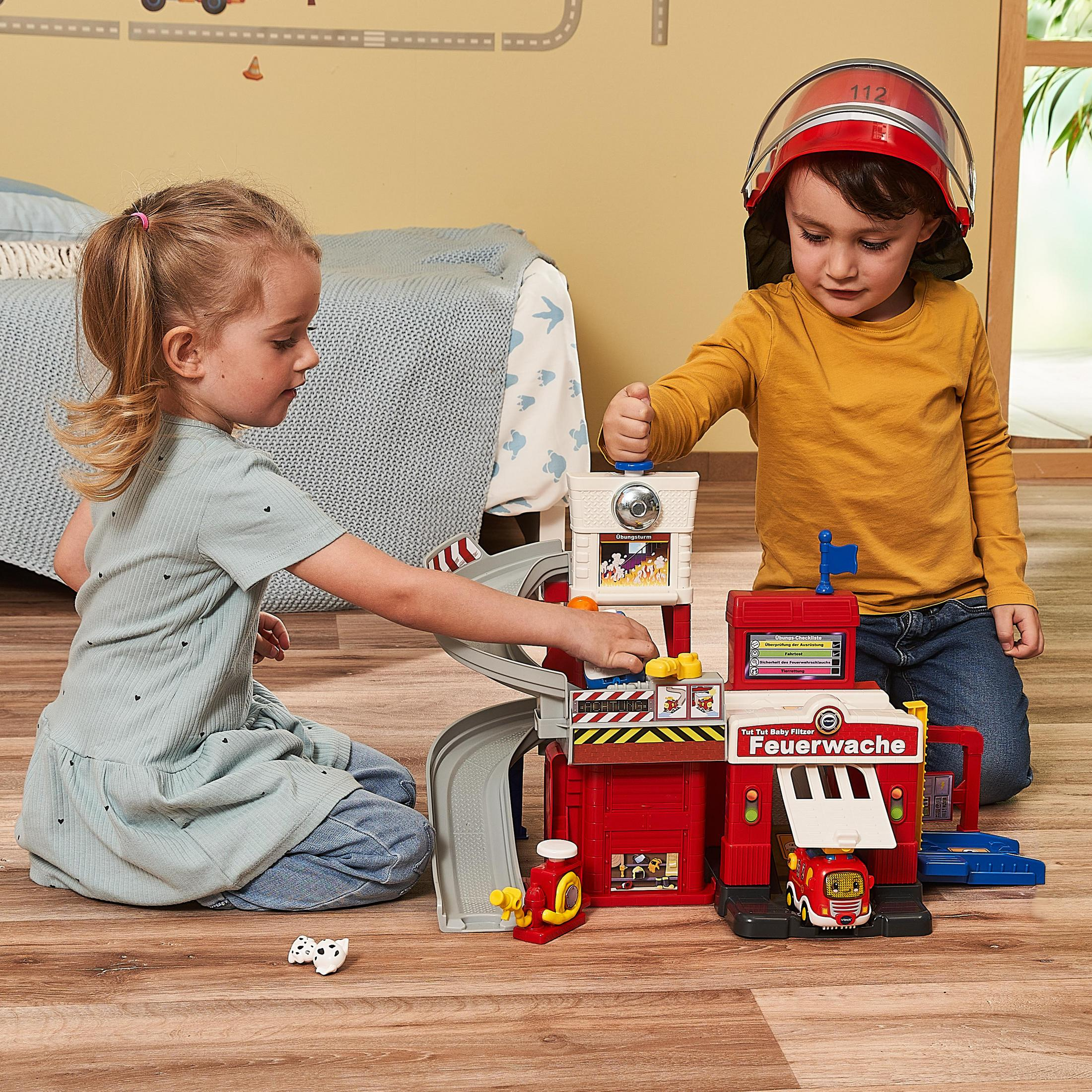 Zwei Kinder spielen mit einem Spielzeug-Feuerwehrhaus-Set, einschließlich eines Autos und eines Spielzeug-Feuerwehrhelms.