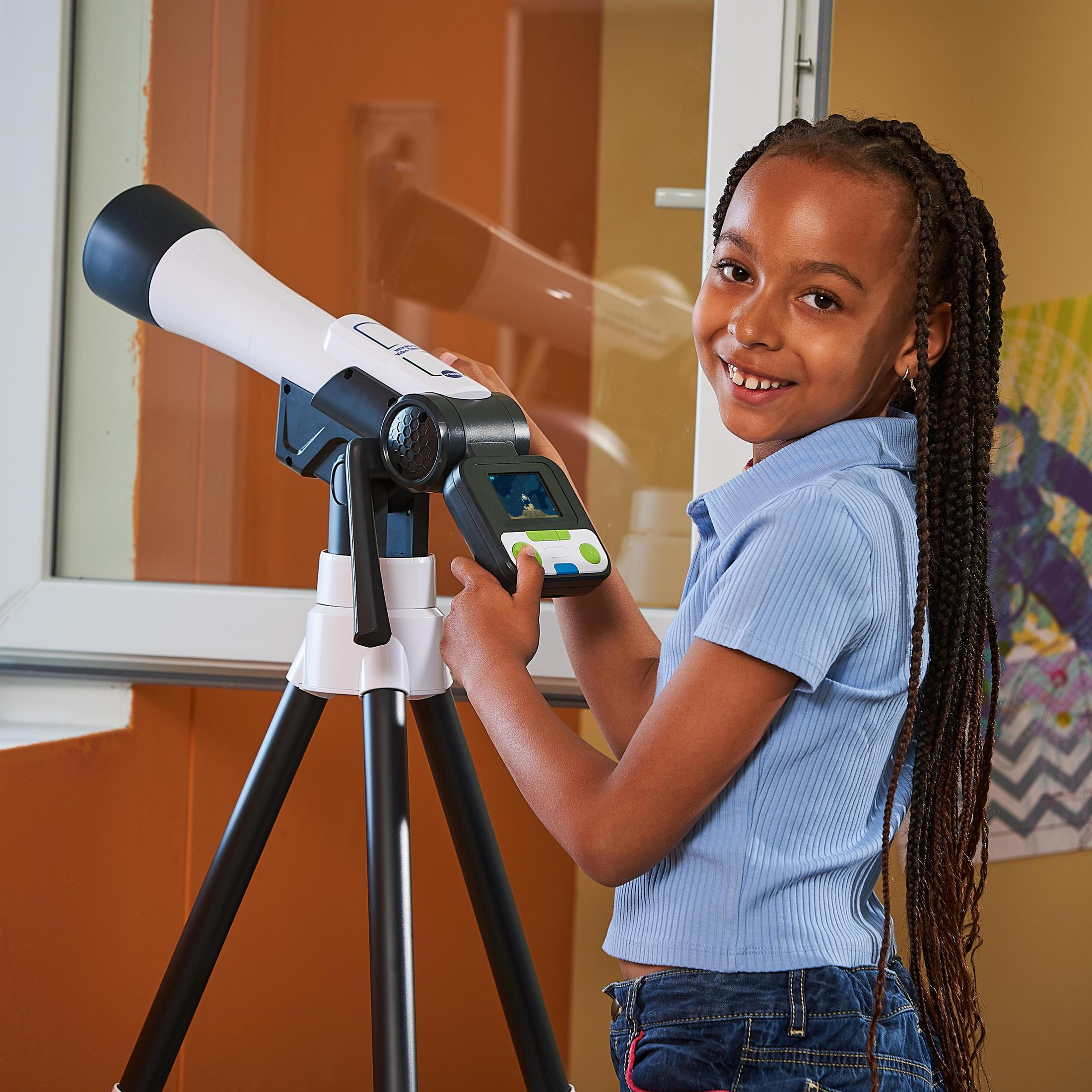 Una ragazza sorridente, che guarda attraverso un telescopio bianco e nero, vicino a una finestra.