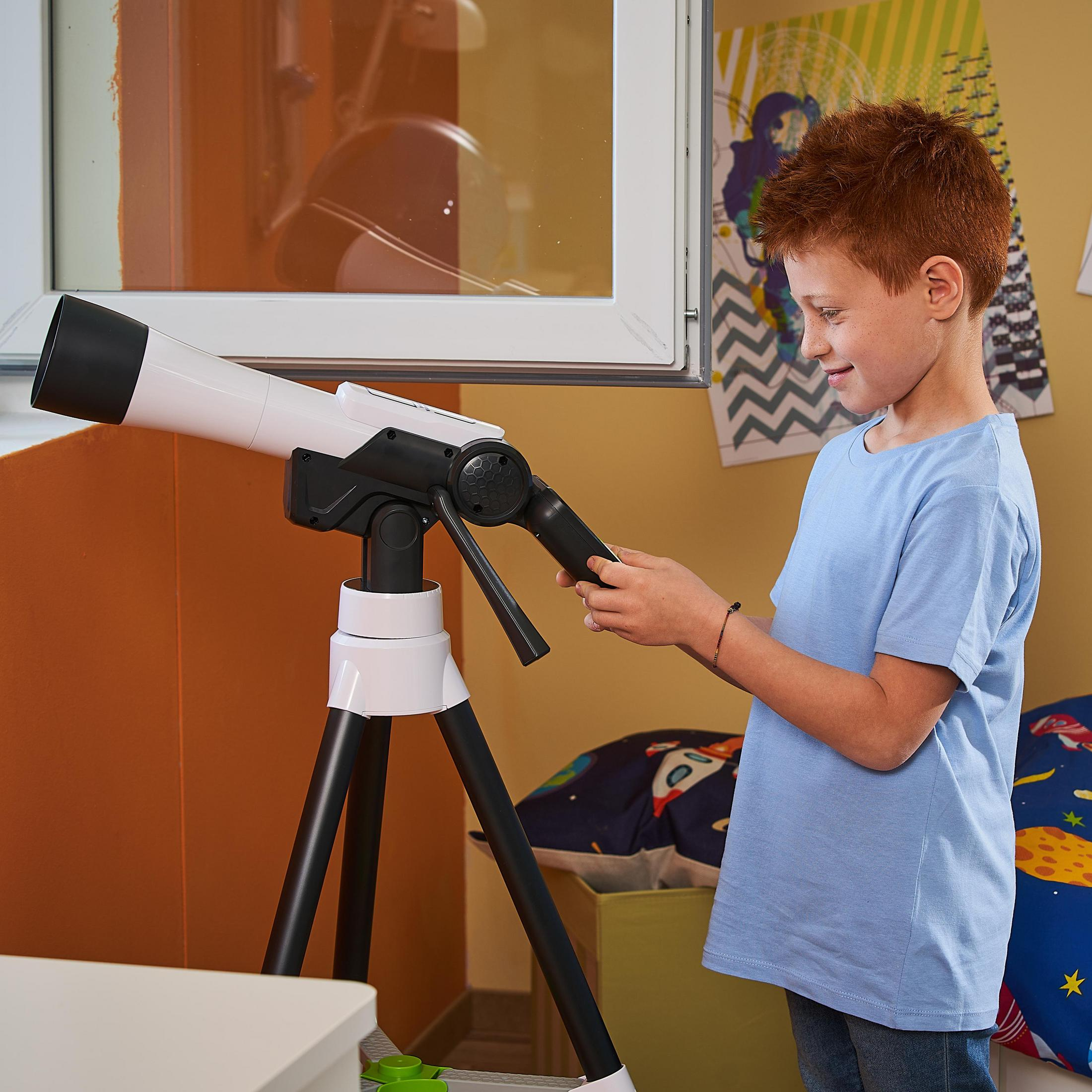 Un ragazzo con un telescopio. Sta guardando nel telescopio. Telescopio bianco e nero su un treppiede. Sfondo giallo del muro.