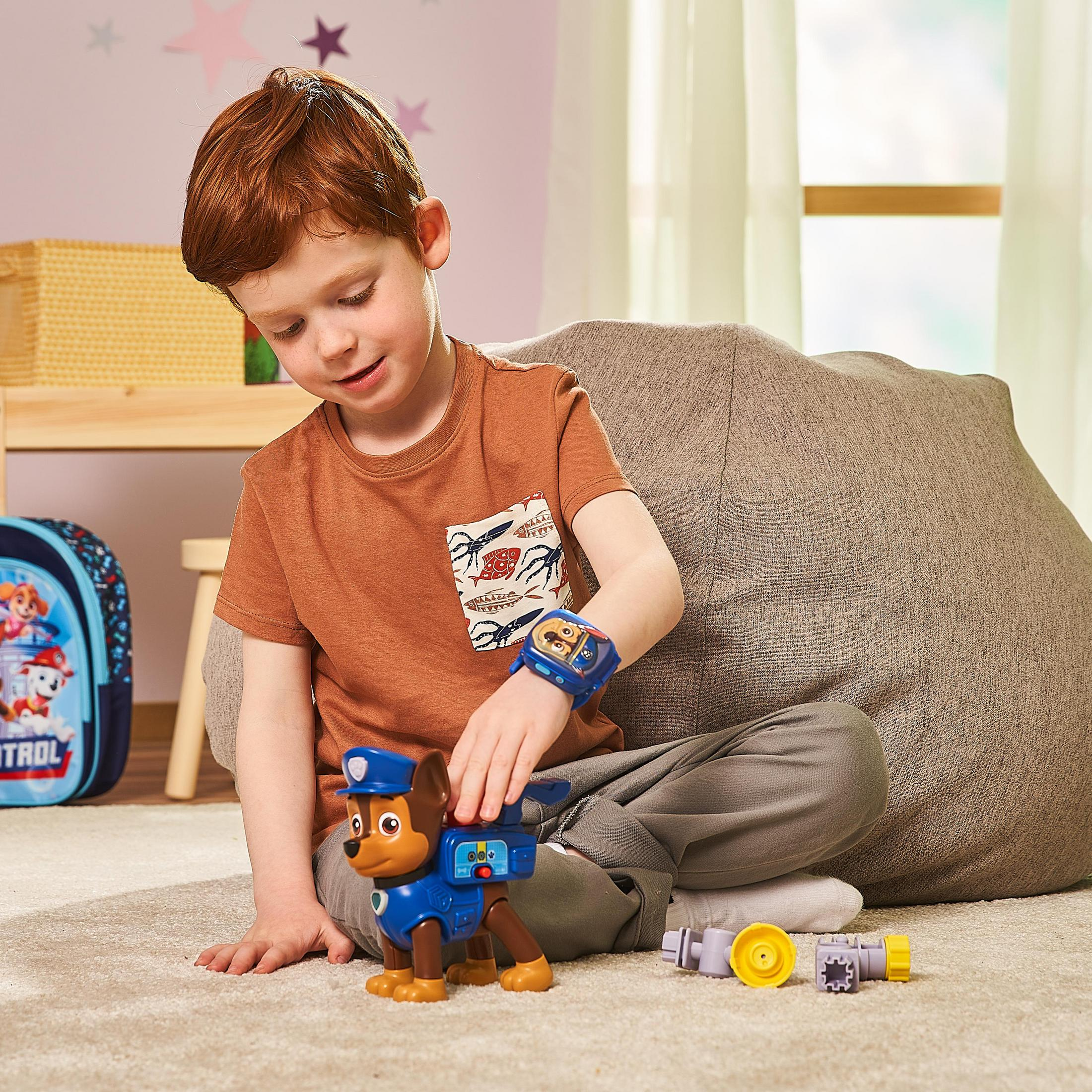 Ein Kind trägt eine Paw Patrol-Uhr und spielt mit einem Spielzeughund und Zahnrädern.