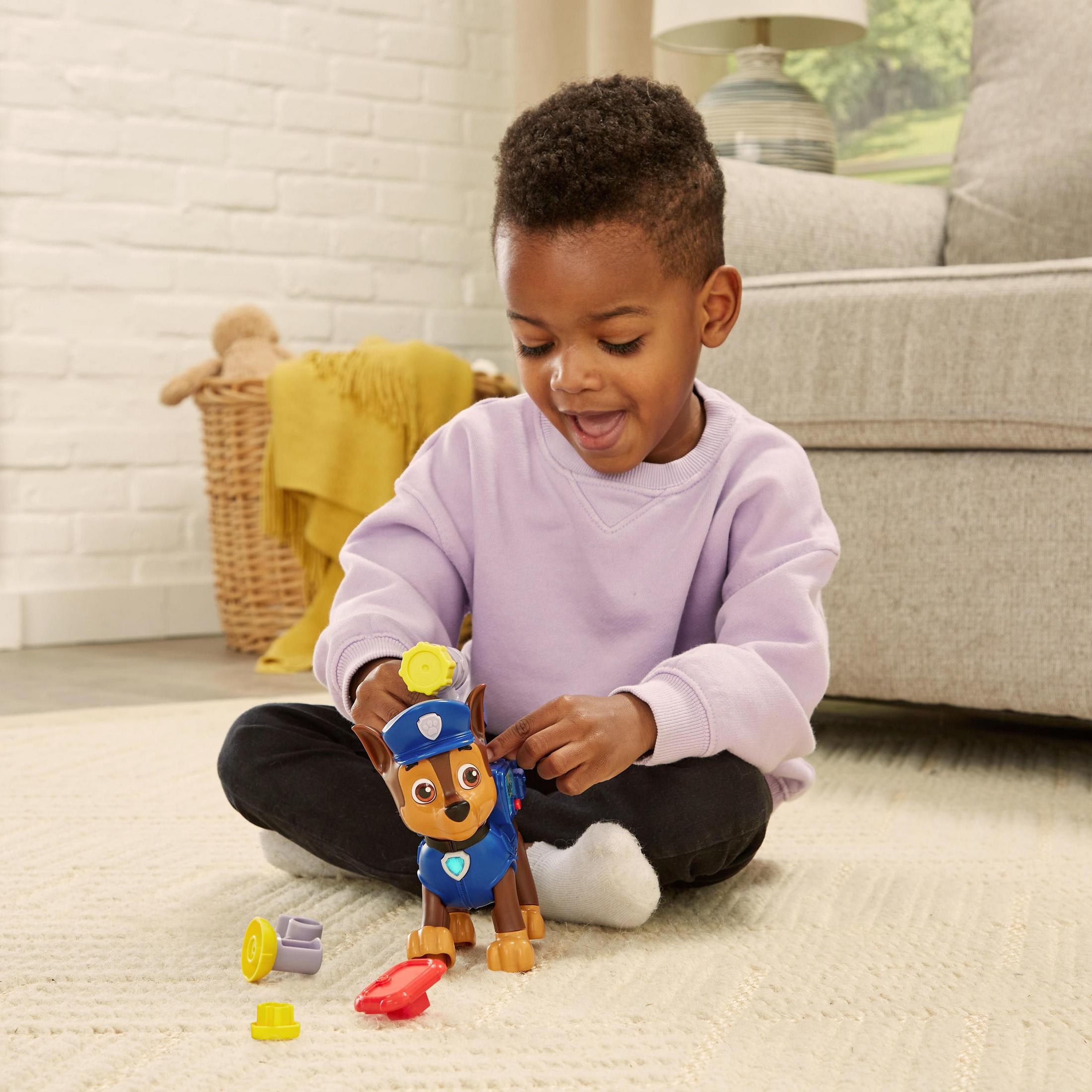 Ein kleiner Junge sitzt auf einem Teppich und spielt mit einem Spielzeug eines braunen und blauen Hundes mit blauem Hut.