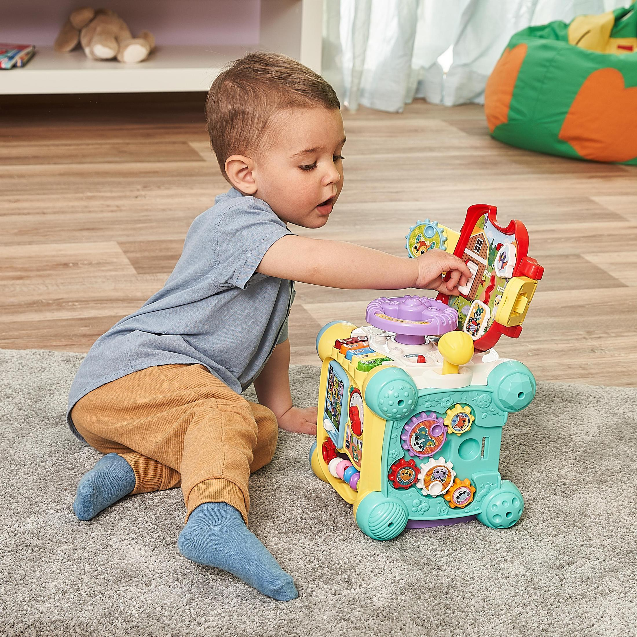 Ein Baby spielt mit einem bunten Spielzeugwürfel. Das Baby trägt ein blaues Hemd und eine braune Hose.